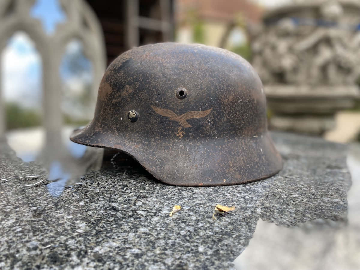 Ww2 桌布 壁紙 — 一個生鏽的二戰德國軍用頭盔，帶有鷹徽，放在墓地潮濕的花崗岩墓碑上。