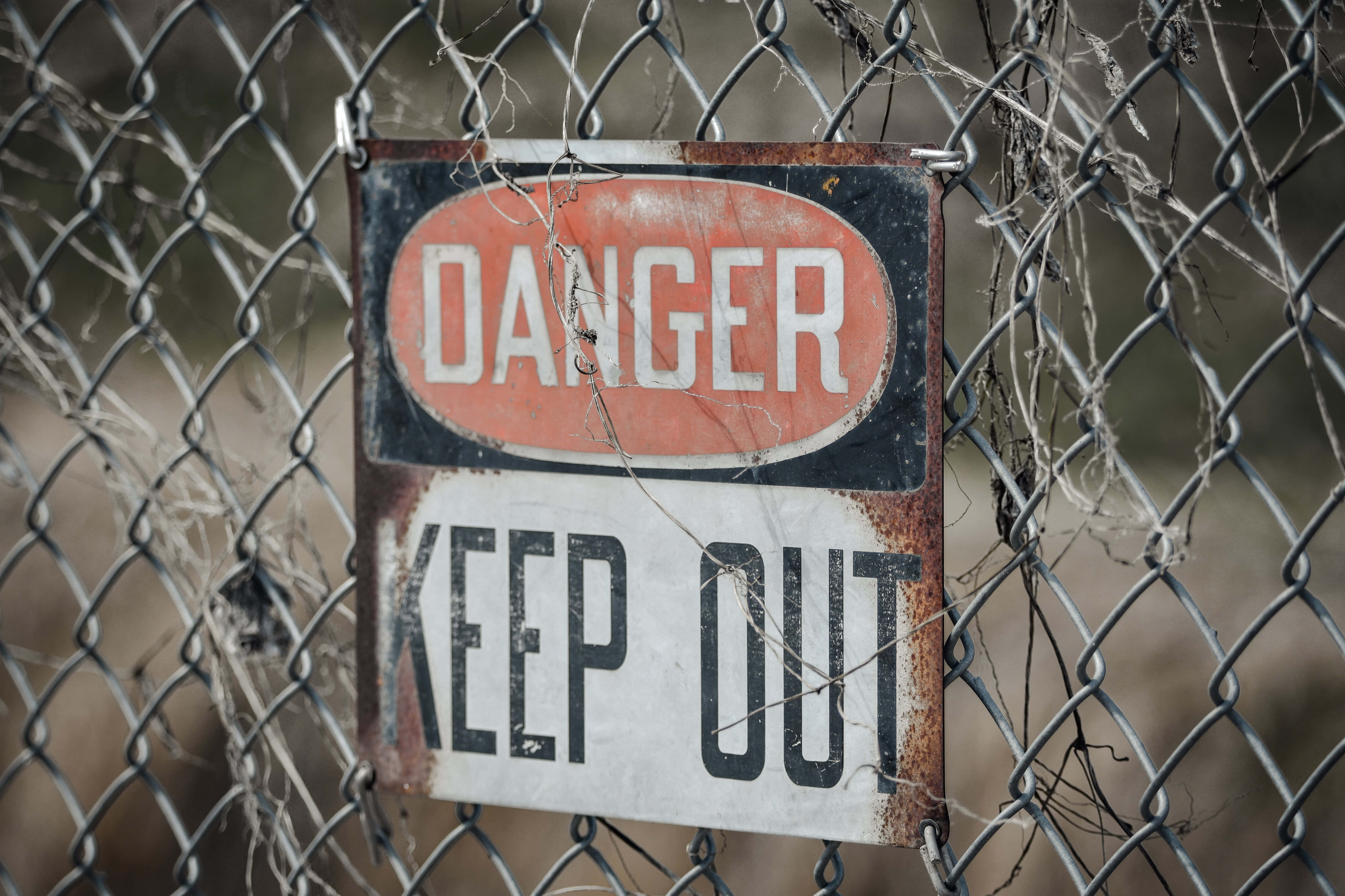 Danger 桌布 壁紙 — 一個生鏽的危險禁止進入標誌掛在纏繞著乾枯藤蔓的鐵絲網圍欄上。