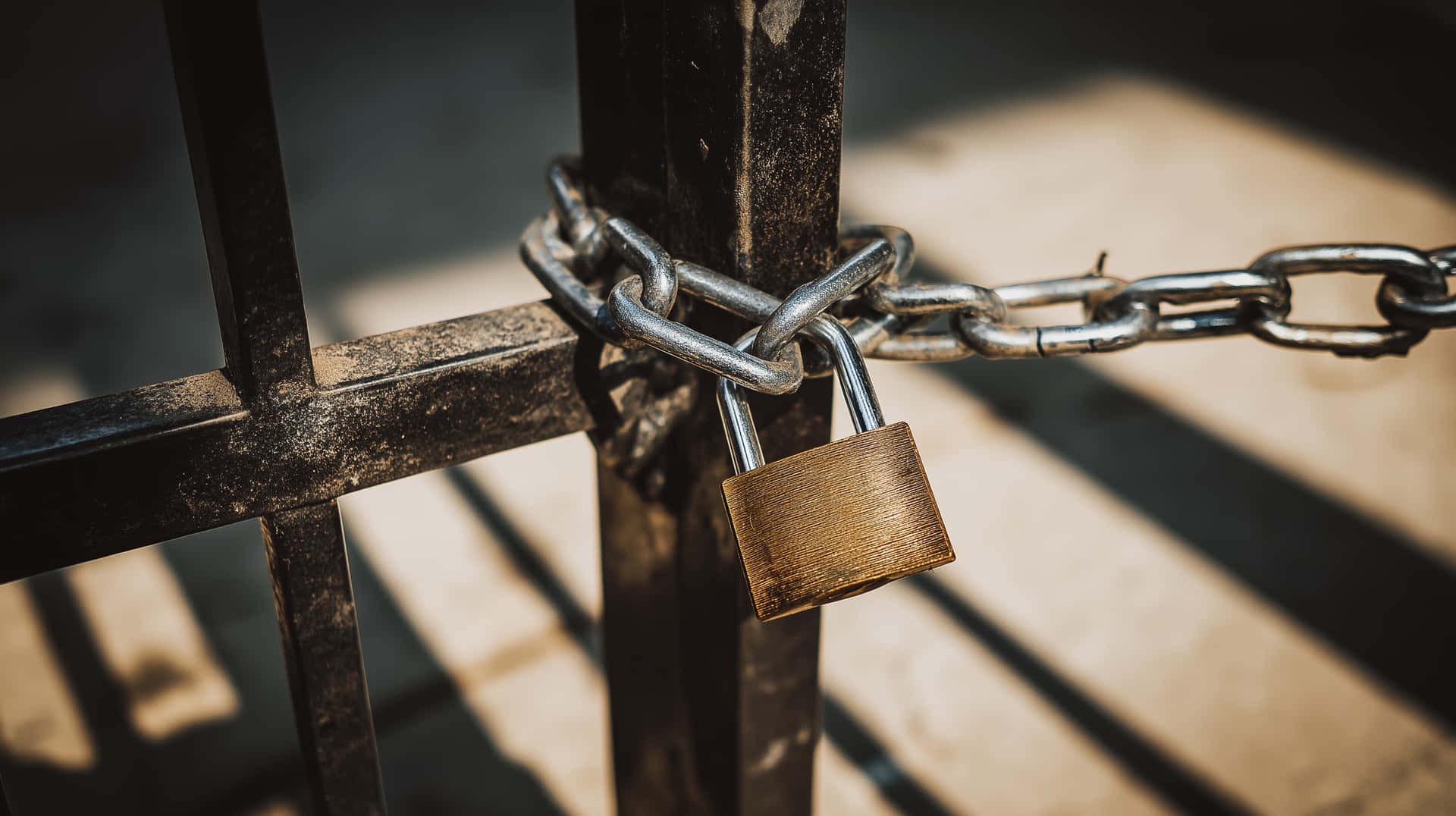 Industrial Gate Secured with Heavy Chain and Padlock 壁紙 — 一個生鏽的掛鎖用重鏈鎖住一個風化的金屬閘門，溫暖的陽光投下銳利的陰影。