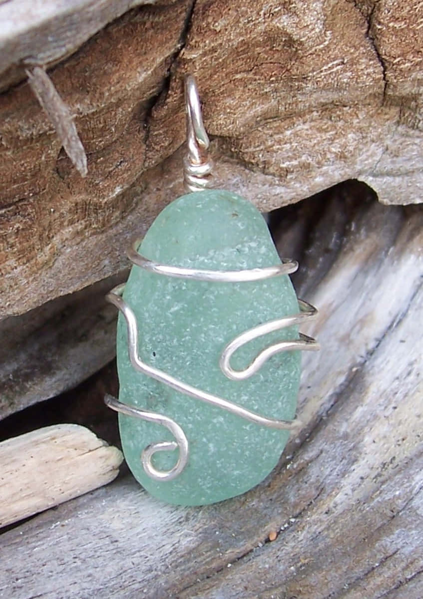 Sea Glass 桌布 壁紙 — 一個用銀線包裹的海玻璃吊墜，靠在風化的浮木和岩石上。