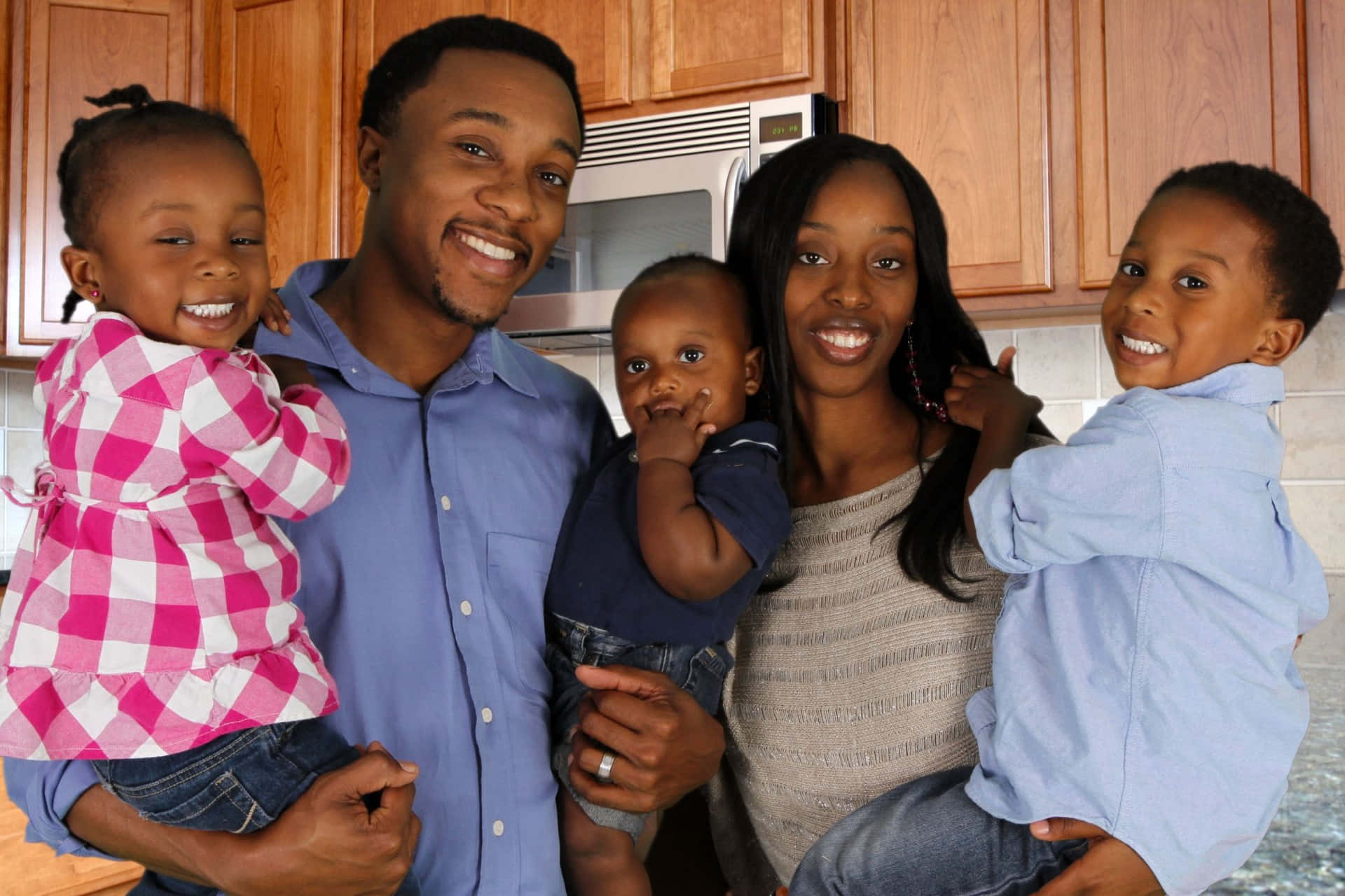 Black Family 桌布 壁紙 — 一個由五人組成的快樂非裔美國家庭在一個配有木製櫥櫃和微波爐的舒適廚房裡溫暖地微笑。