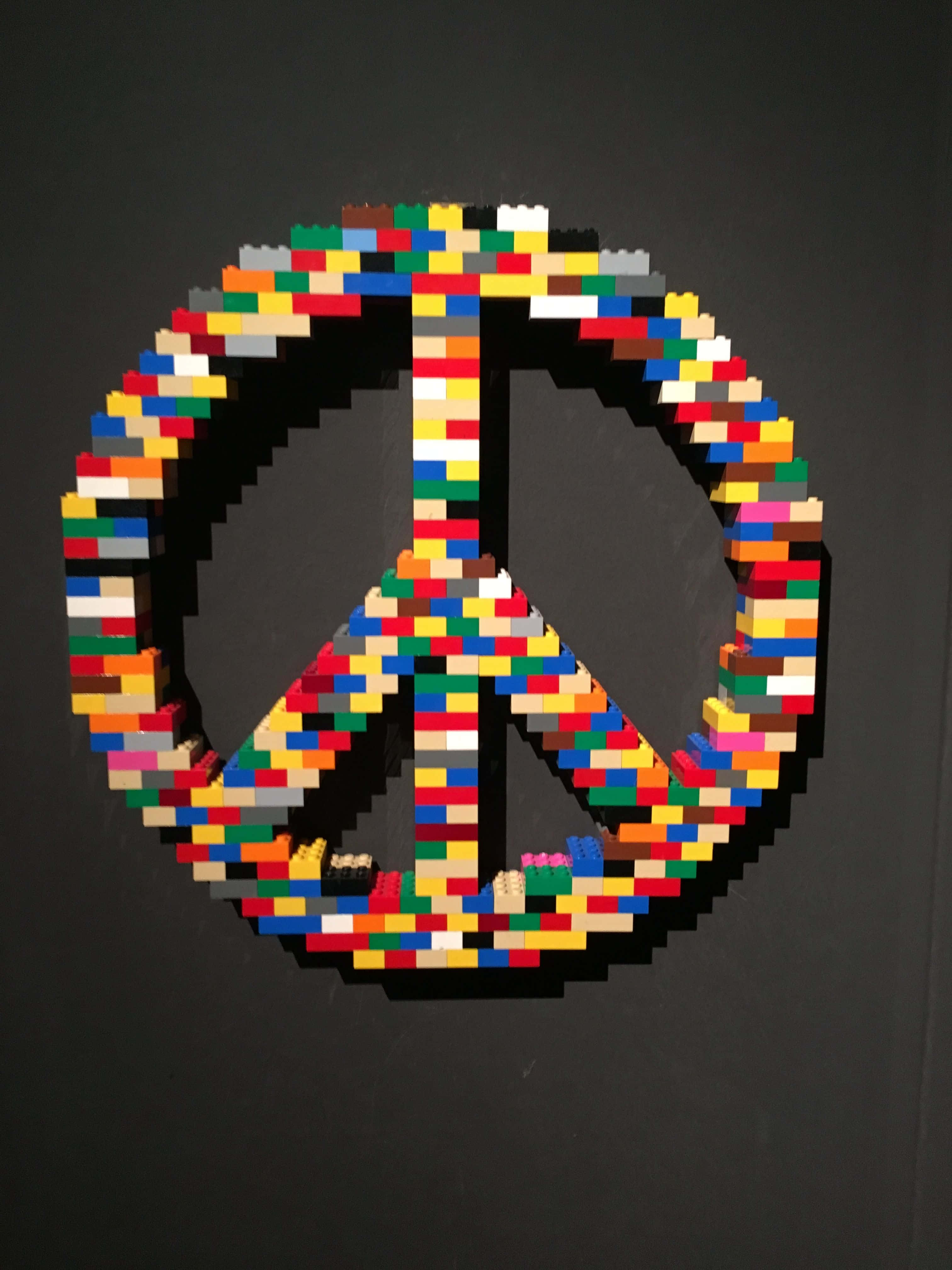 Lego Art 桌布 壁紙 — 一個由多色LEGO積木製成的鮮明和平標誌，在深灰色牆壁上格外突出。