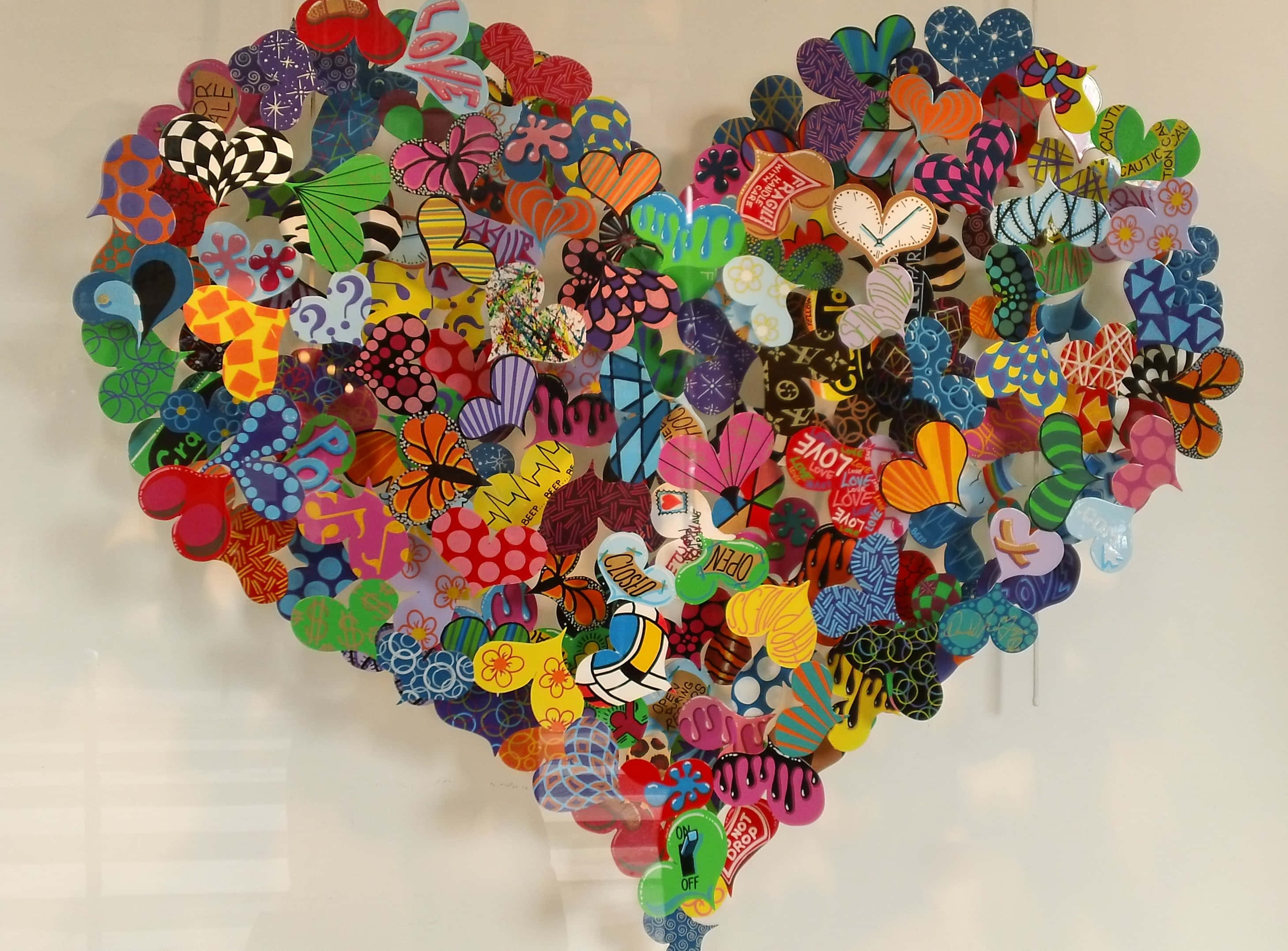 Heart Art 桌布 壁紙 — 一個由彩色圖案紙心形和蝴蝶組成的充滿活力的心形拼貼畫裝飾著樸素的牆壁。