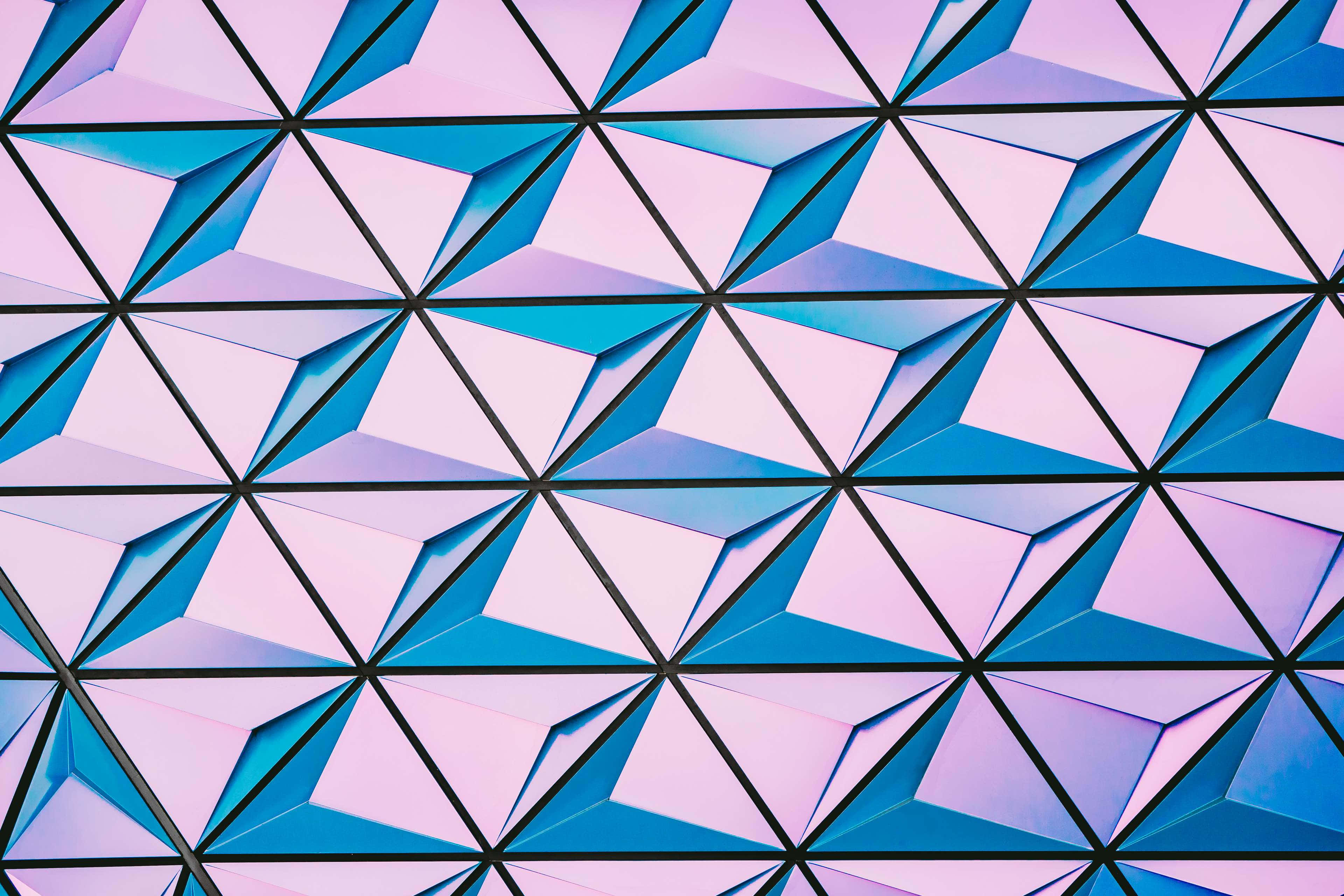 Geometric Shapes 桌布 壁紙 — 一個由柔和粉紅色和藍色色調的互鎖三角形組成的幾何圖案，搭配大膽的黑色線條，創造出現代建築紋理。