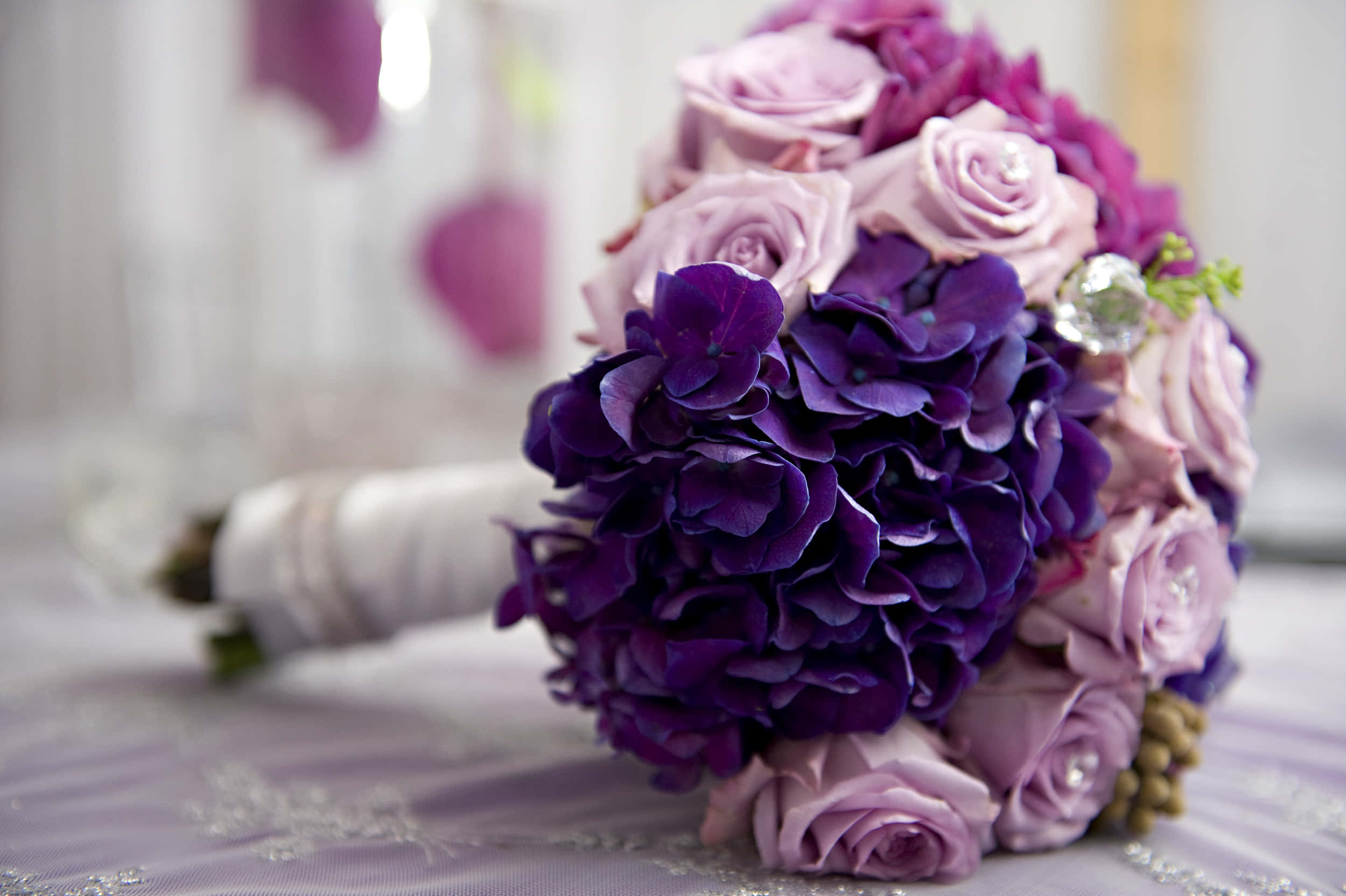 Wedding Bouquet 桌布 壁紙 — 一個由深紫色繡球花和柔軟的薰衣草玫瑰組成的豐盛新娘花束，飾有水晶，放在相配的紫色蕾絲桌布上。