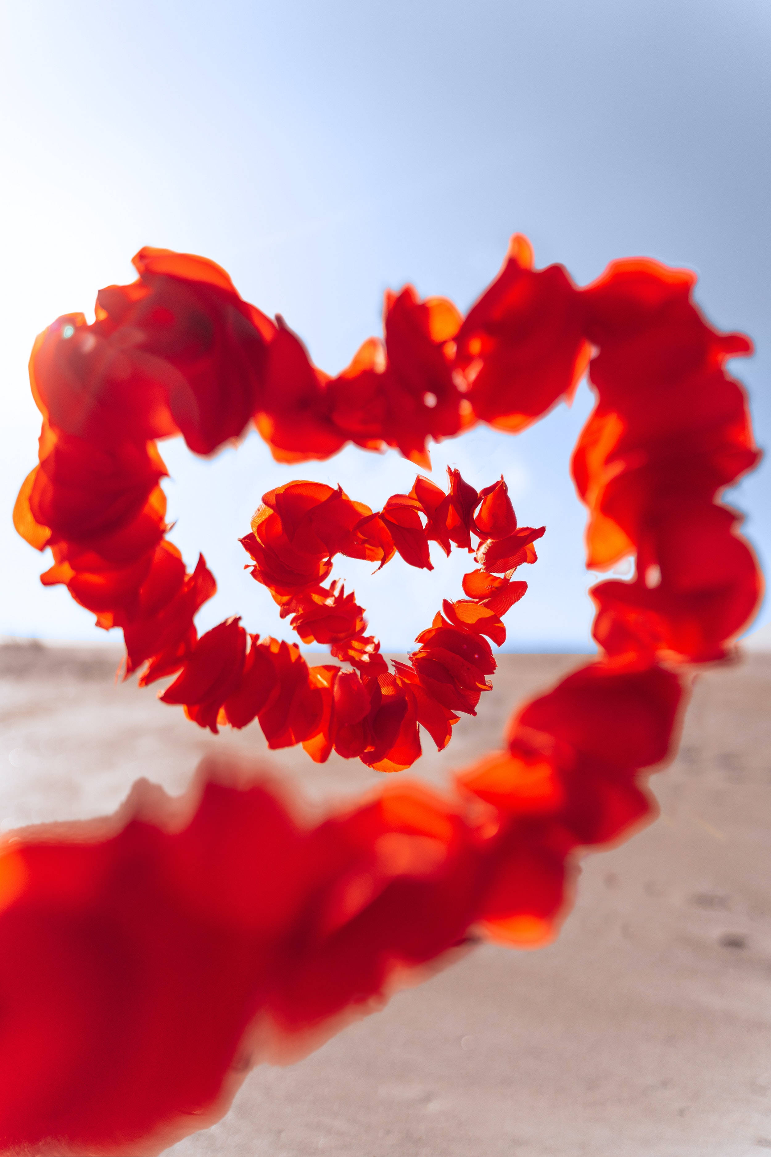 Romantic Love 桌布 壁紙 — 一個由熱帶花卉組成的鮮紅色心形花環，在沙灘上清澈的藍天下格外突出。