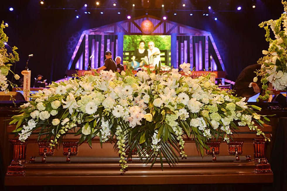 Funeral 桌布 壁紙 — 一個由白色和綠色花朵組成的大型花卉佈置，在莊嚴的室內追悼會上裝飾著一個拋光的木製棺材。