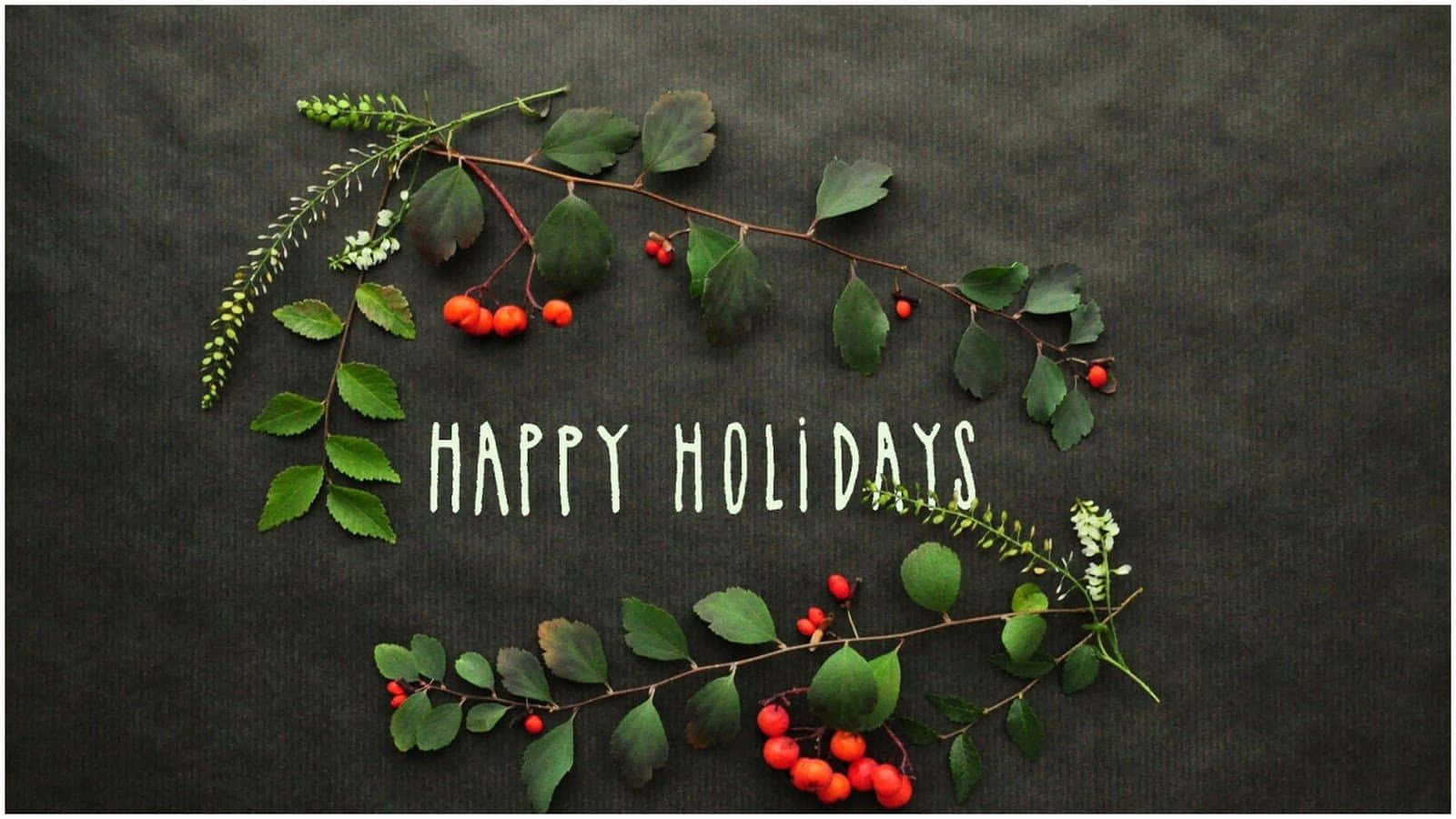Happy Holidays 桌布 壁紙 — 一個由綠色樹枝、紅色漿果和白色花朵組成的節日花環，在深色紋理背景上圍繞著手寫文字「HAPPY HOLIDAYS」。