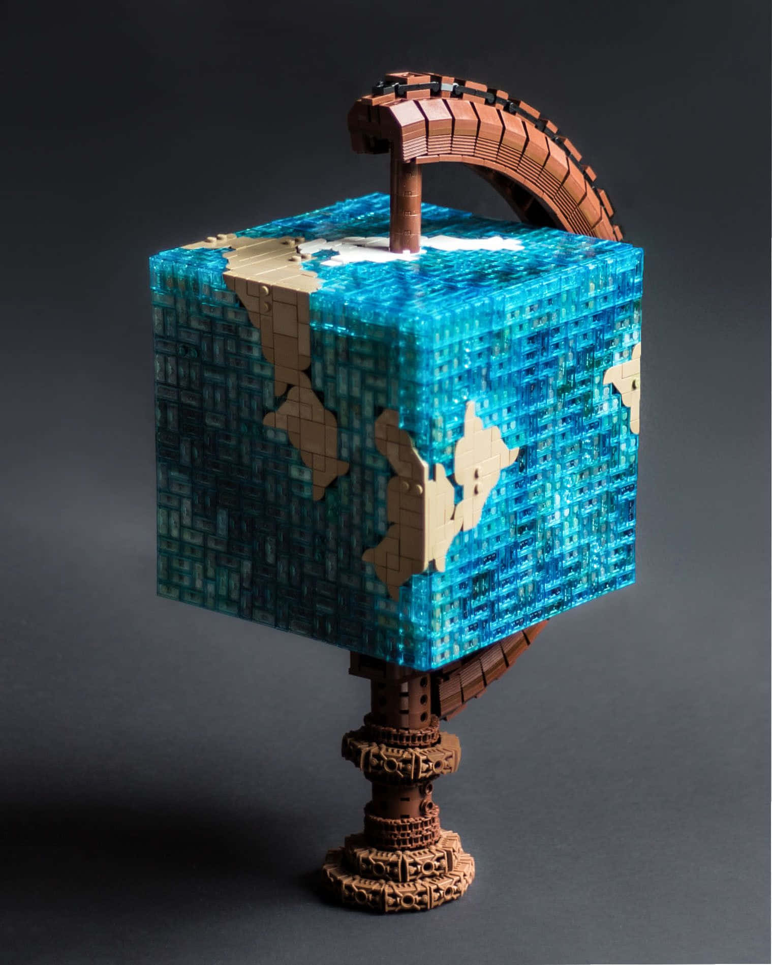 Lego Art 桌布 壁紙 — 一個由藍色和米色馬賽克瓷磚製成的立方體，描繪了地球的大陸，放置在一個帶有彎曲拱形手柄的華麗棕色底座上。
