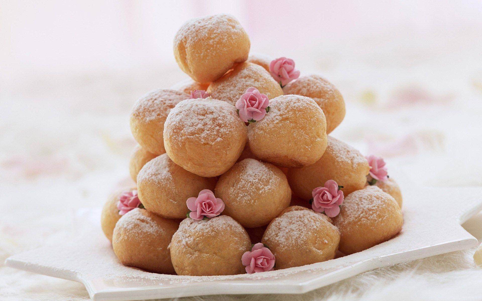 Desserts 桌布 壁紙 — 一個由金色泡芙堆成的金字塔，撒上糖粉，並以精緻的粉紅色糖玫瑰點綴，放在白色盤子上。