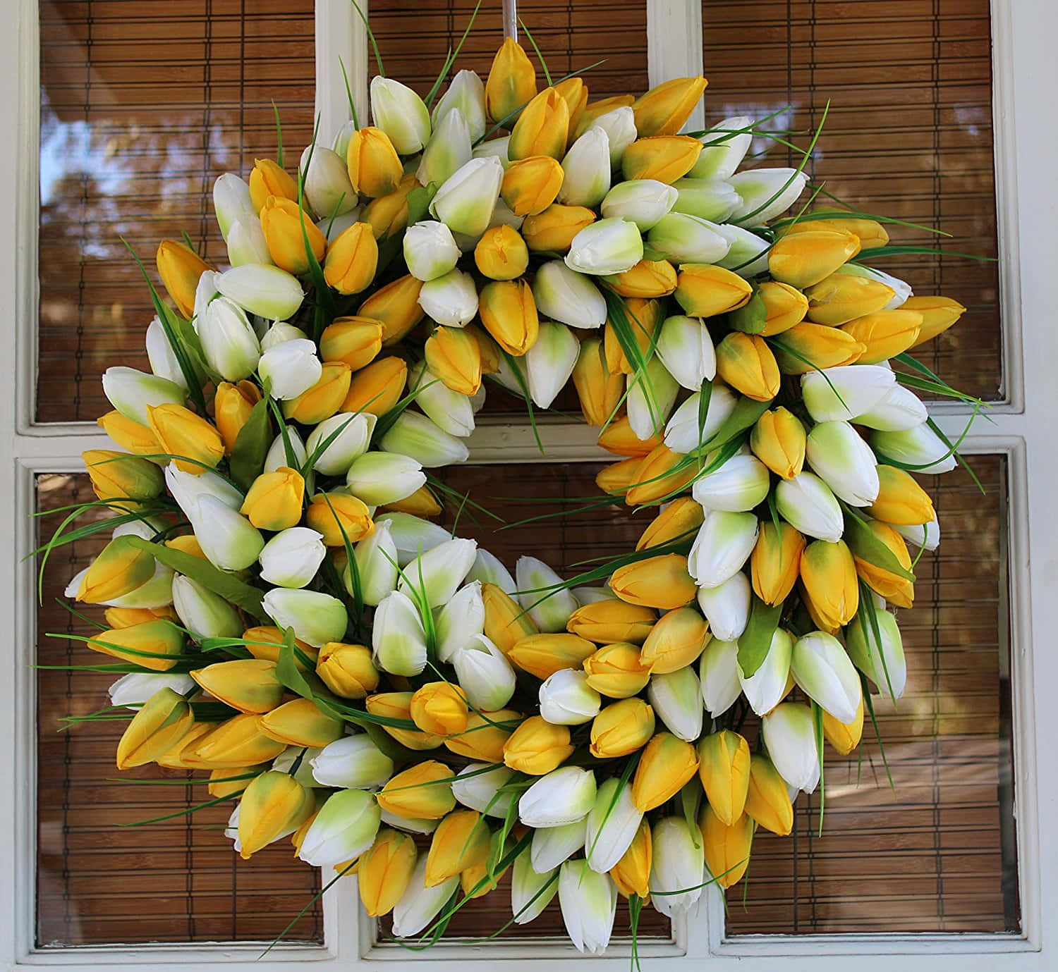 Spring Wreaths 桌布 壁紙 — 一個由黃色和白色鬱金香組成的鮮豔花環，帶有綠色莖，掛在帶有竹簾的玻璃門上。