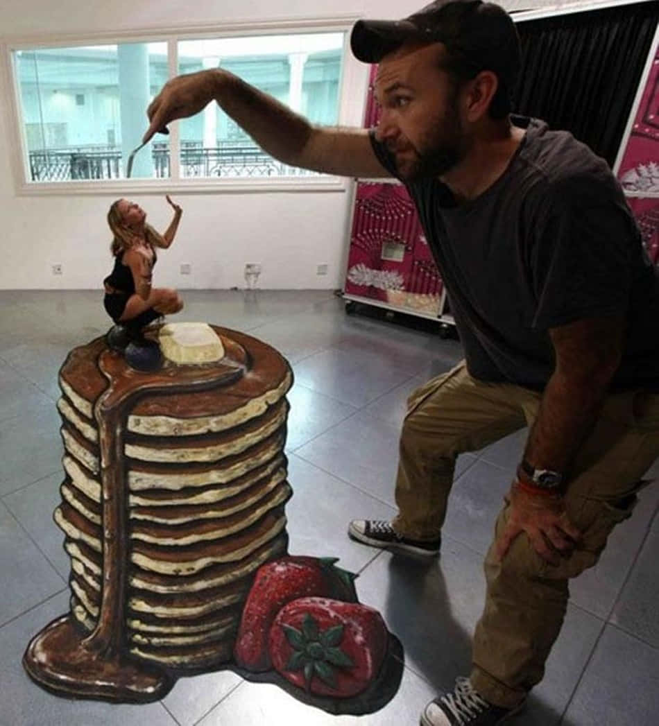 odd 桌布 壁紙 — 一個男人俯身於瓷磚地板上的巨型3D粉筆畫，畫中有煎餅、糖漿和草莓。