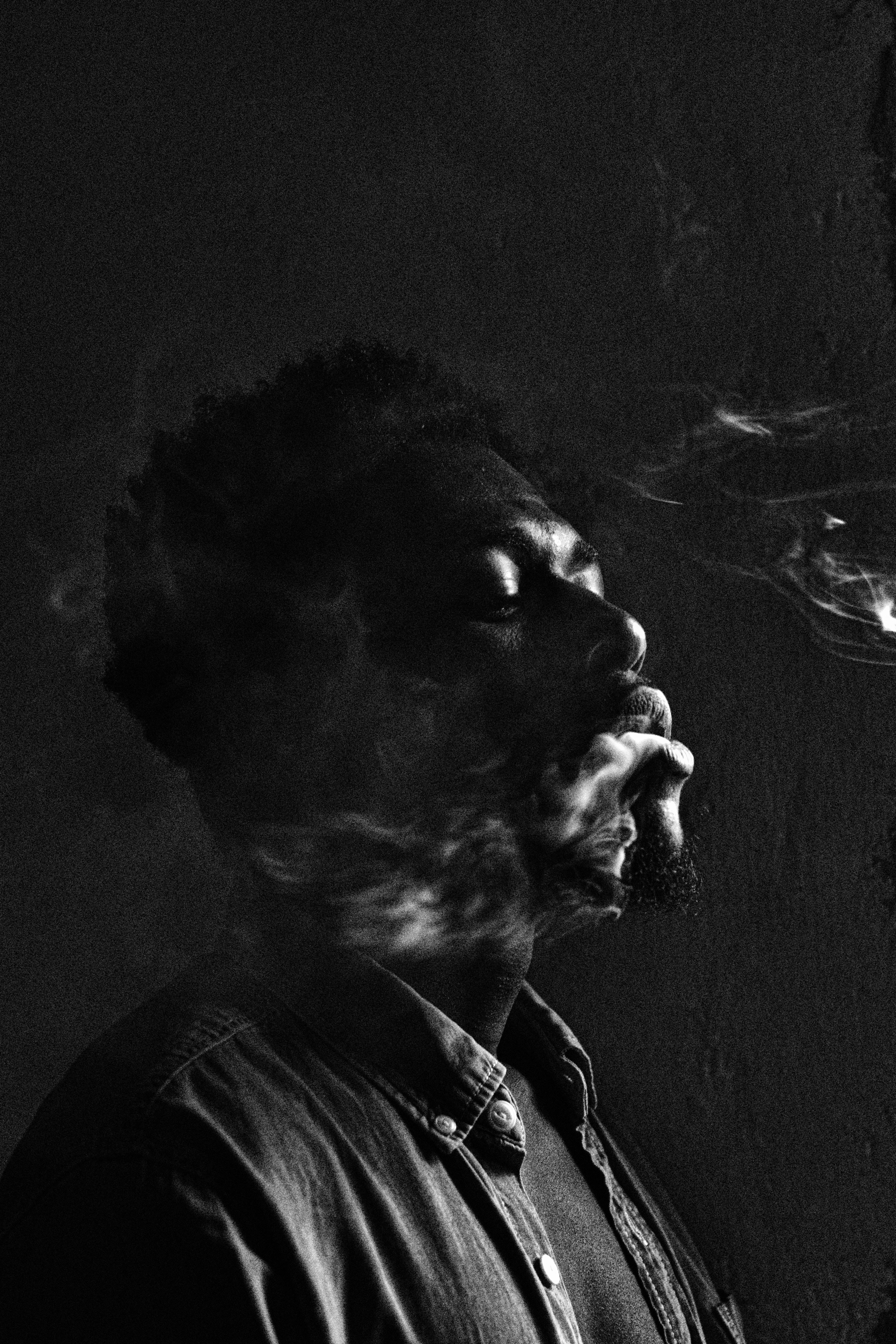Smoking 桌布 壁紙 — 一個男人側面輪廓在黑暗背景下呼出煙霧的高對比黑白肖像。