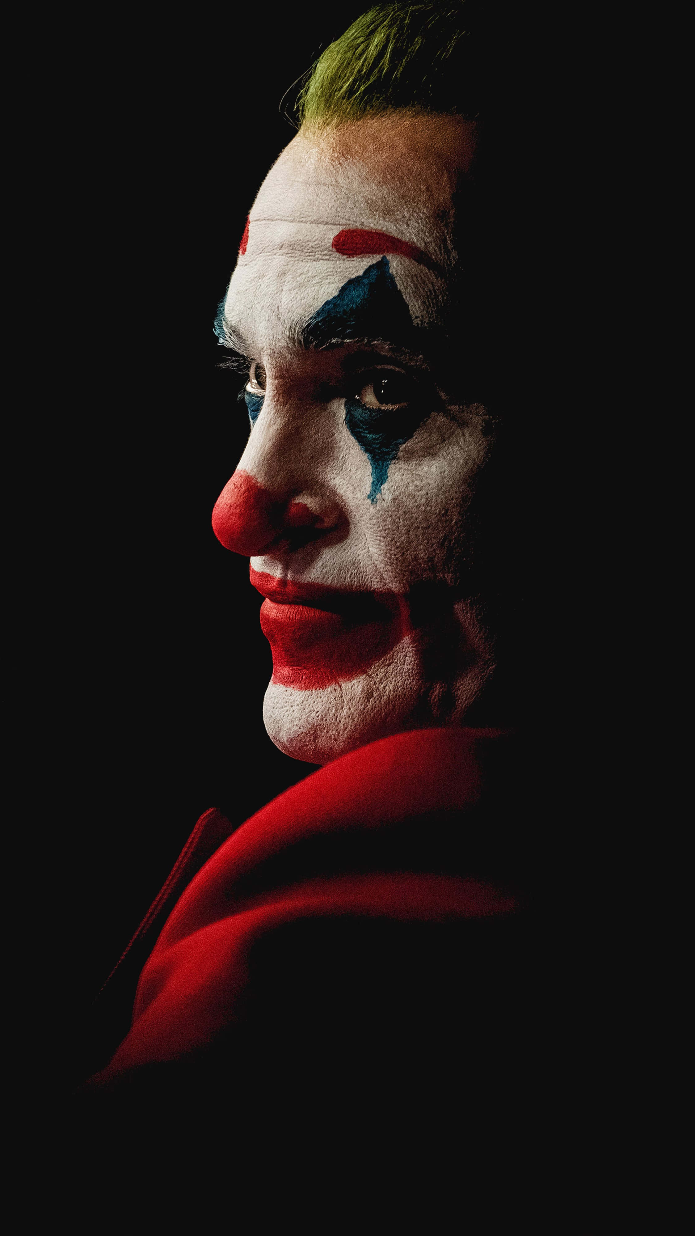 Joker 2019 桌布 壁紙 — 一個男人化著小丑妝，綠色頭髮，身穿紅色外套，在黑色背景前的戲劇性特寫。