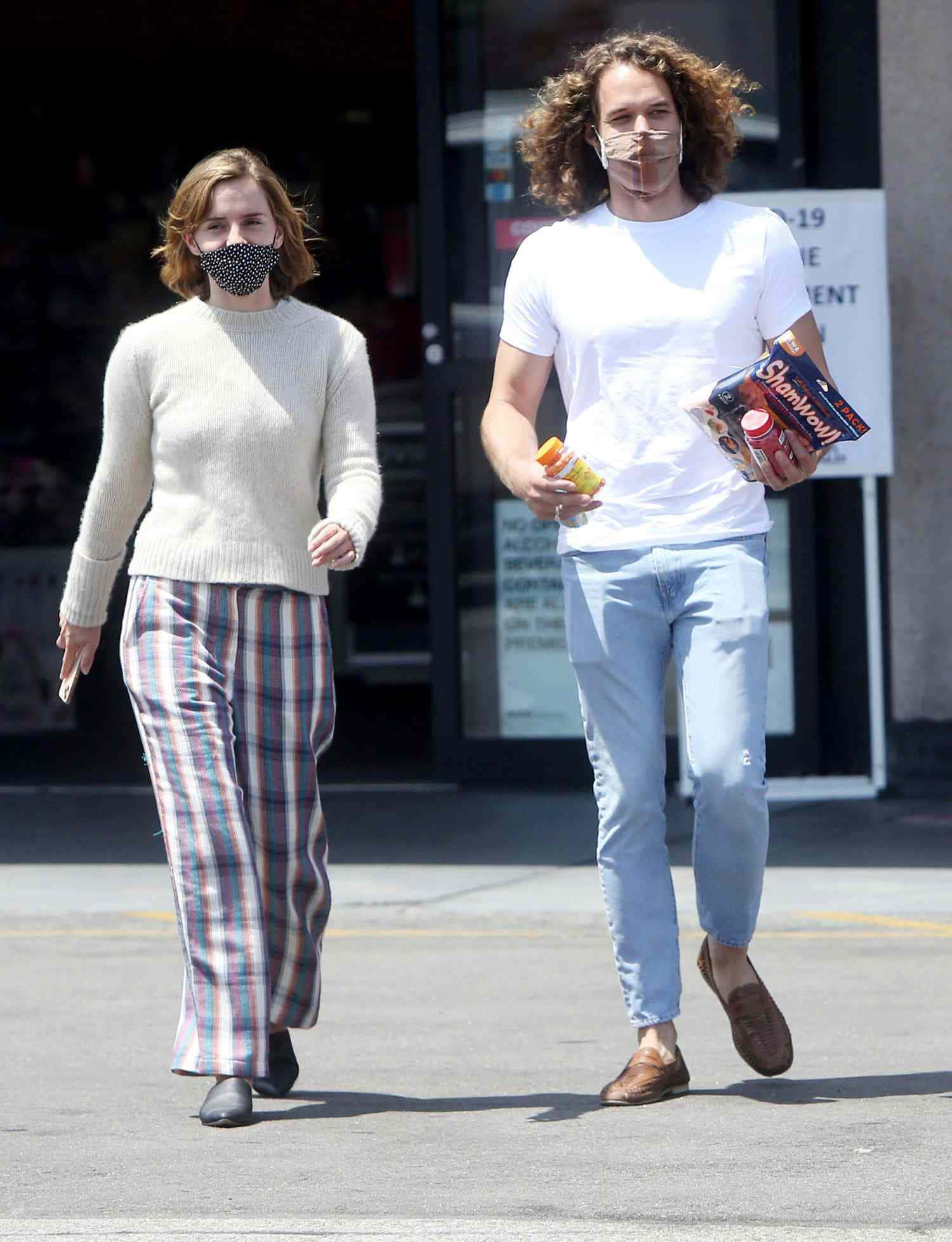 Emma Watson 桌布 壁紙 — 一個男人和女人戴著口罩在陽光明媚的日子裡提著雜貨走在戶外。