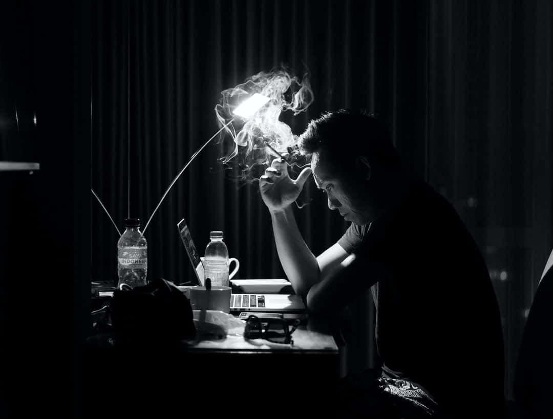 思考 桌布 壁紙 — 一個男人在剪影中，於黑暗房間內一張雜亂的書桌上，在一盞明亮的燈下吸煙。