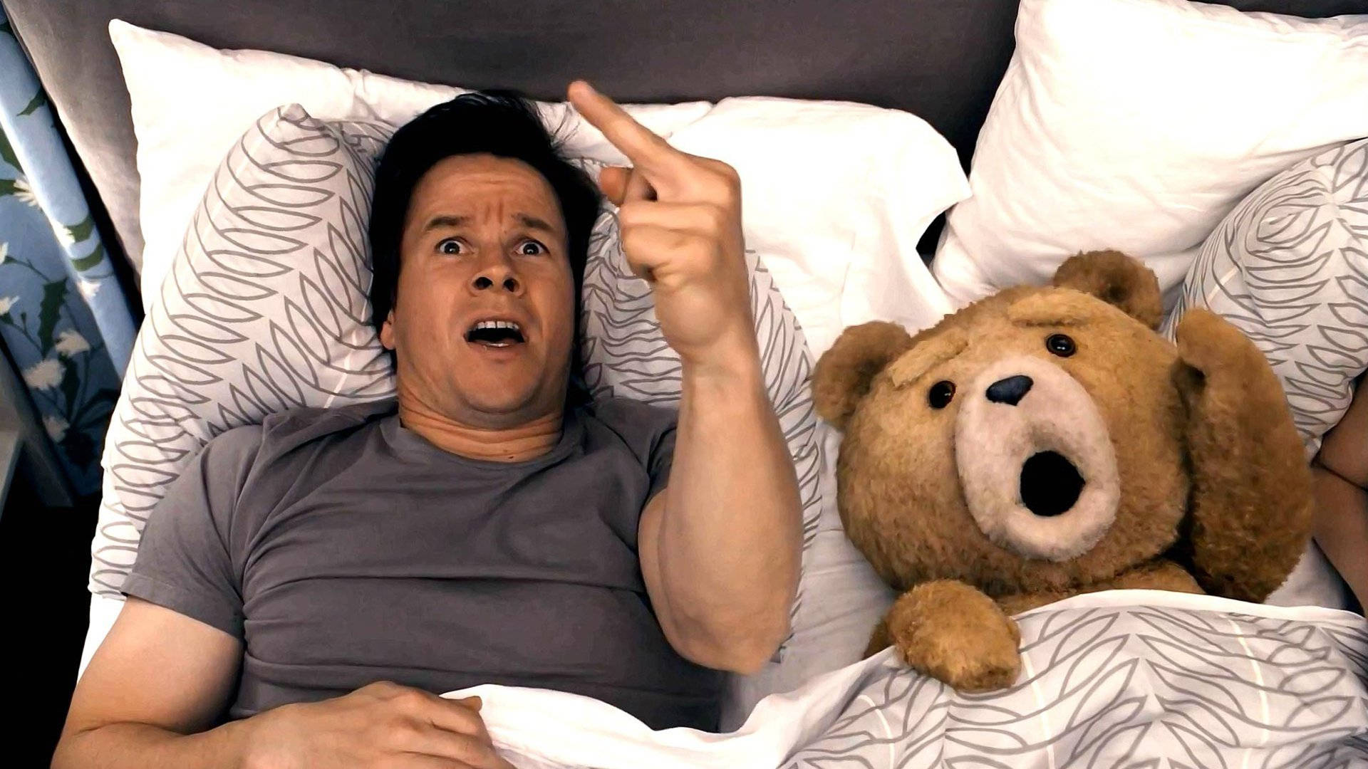 Ted 桌布 壁紙 — 一個男人在床上震驚地指向上方，旁邊有一隻張開嘴巴說話的泰迪熊。