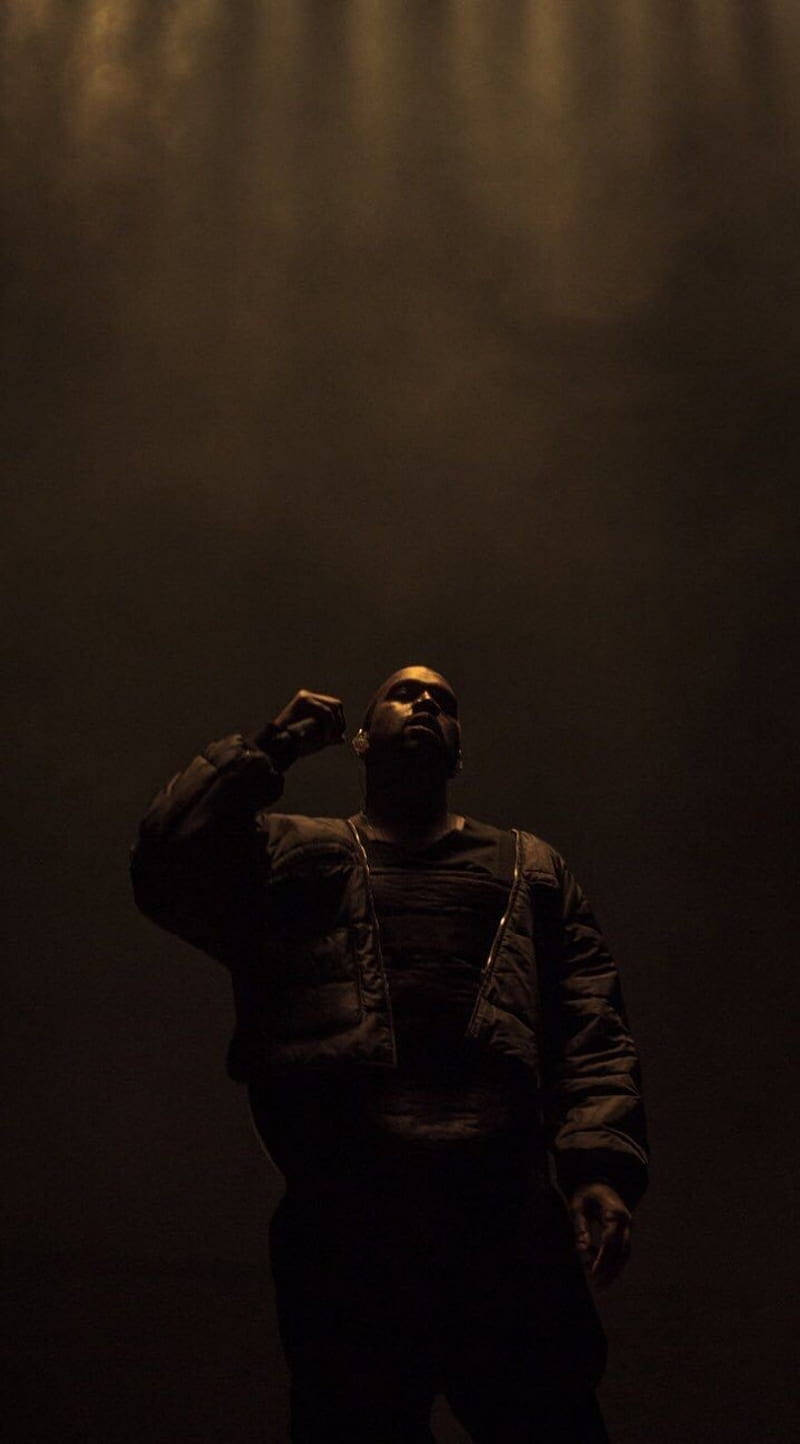 Kanye 桌布 壁紙 — 一個男人在昏暗的光線中站成剪影，一隻手舉到耳邊，背景朦朧黑暗。