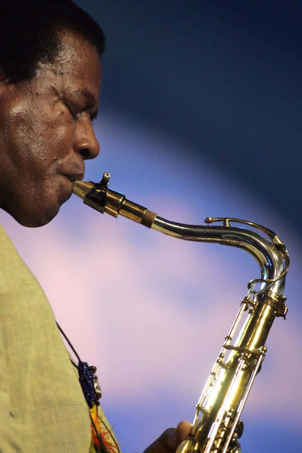 Wayne Shorter 桌布 壁紙 — 一個男人在柔和的紫藍色暮色天空下吹奏金色薩克斯風的特寫。