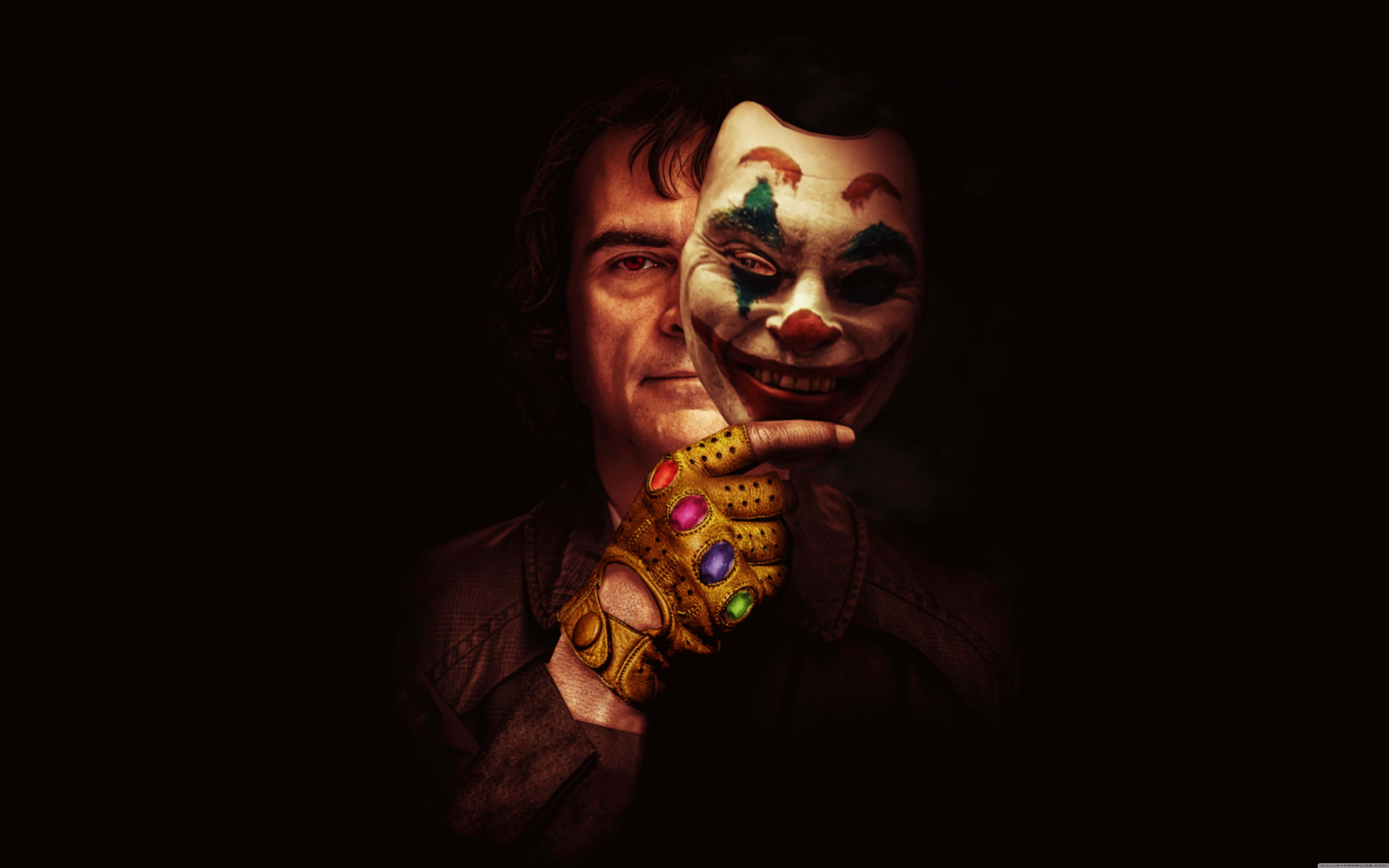 Mask 桌布 壁紙 — 一個男人在黑暗環境中，用戴著鑲有寶石的手套將色彩繽紛的小丑面具貼在臉上。