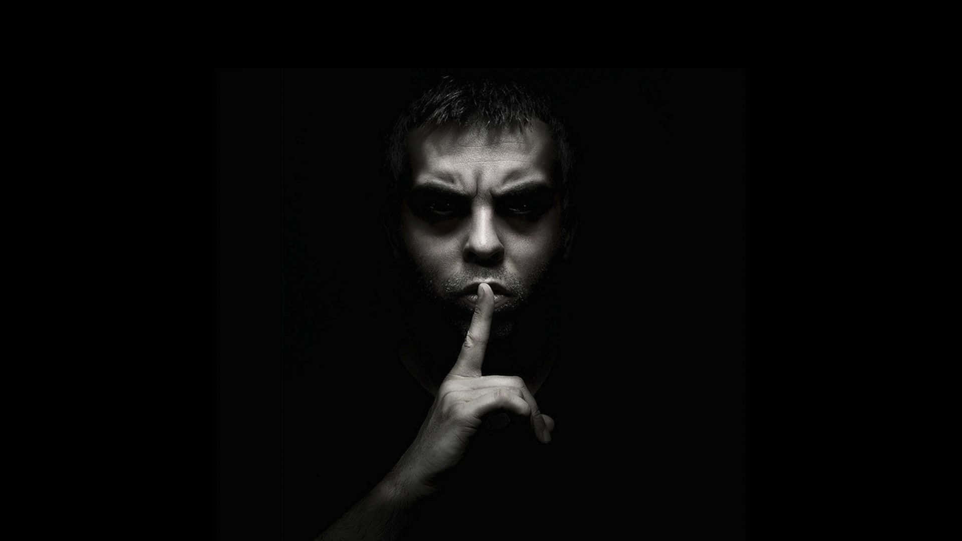 Man 桌布 壁紙 — 一個男人在黑暗的房間裡，在戲劇性的燈光下將手指放在嘴唇上做出安靜的手勢。