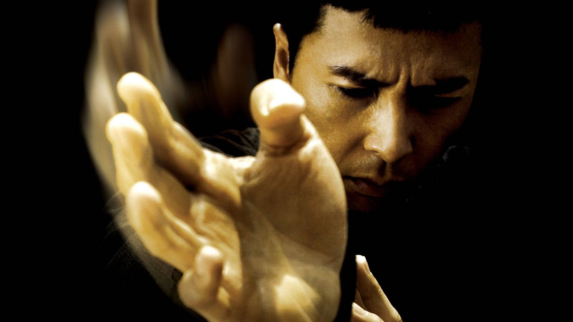 martial arts 桌布 壁紙 — 一個男人在黑暗的環境中向前伸出手，專注而強烈，戲劇性的燈光突顯了他堅定的表情。