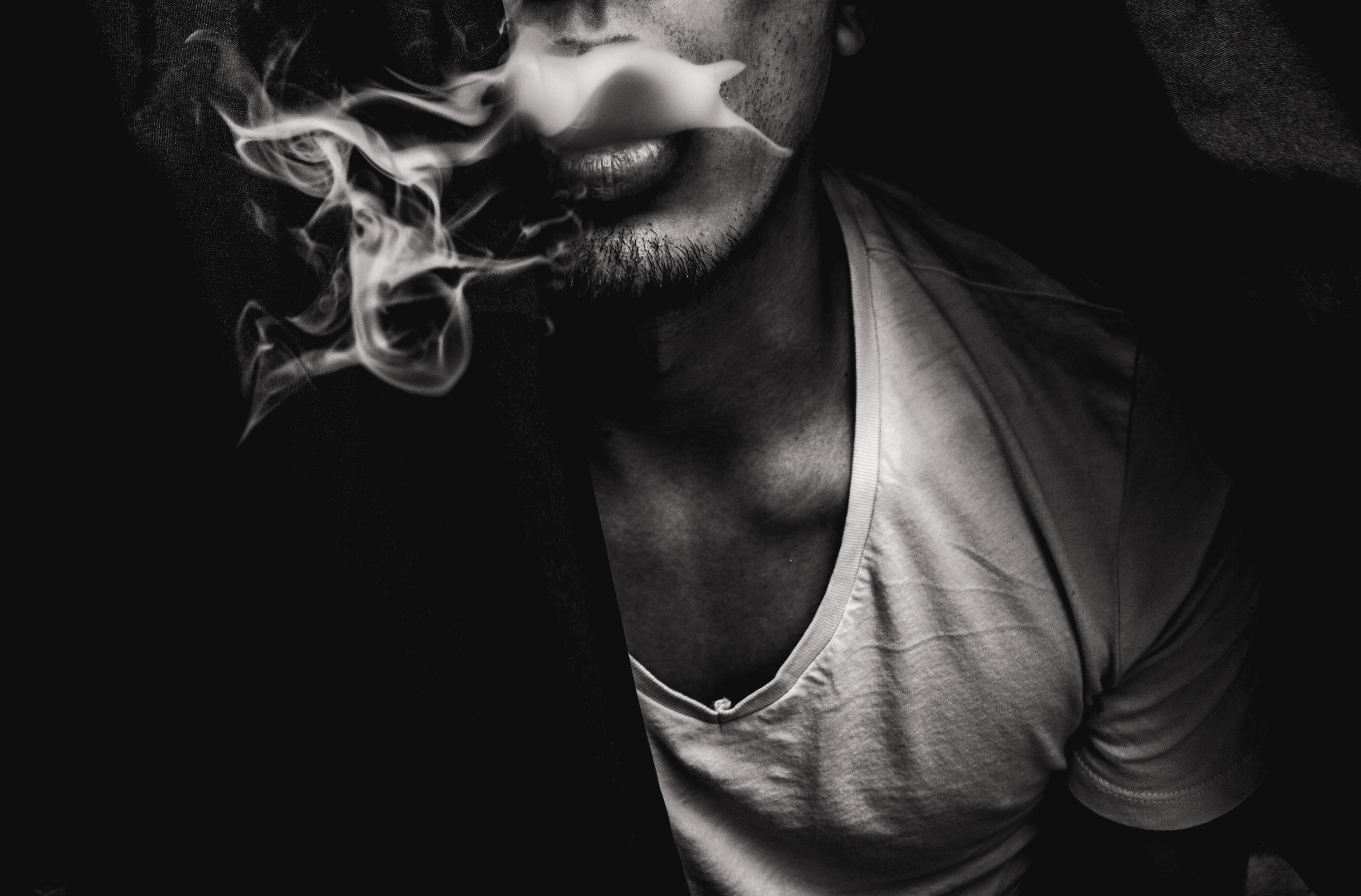 抽菸 桌布 壁紙 — 一個男人在黑暗背景下呼出煙霧的黑白特寫。