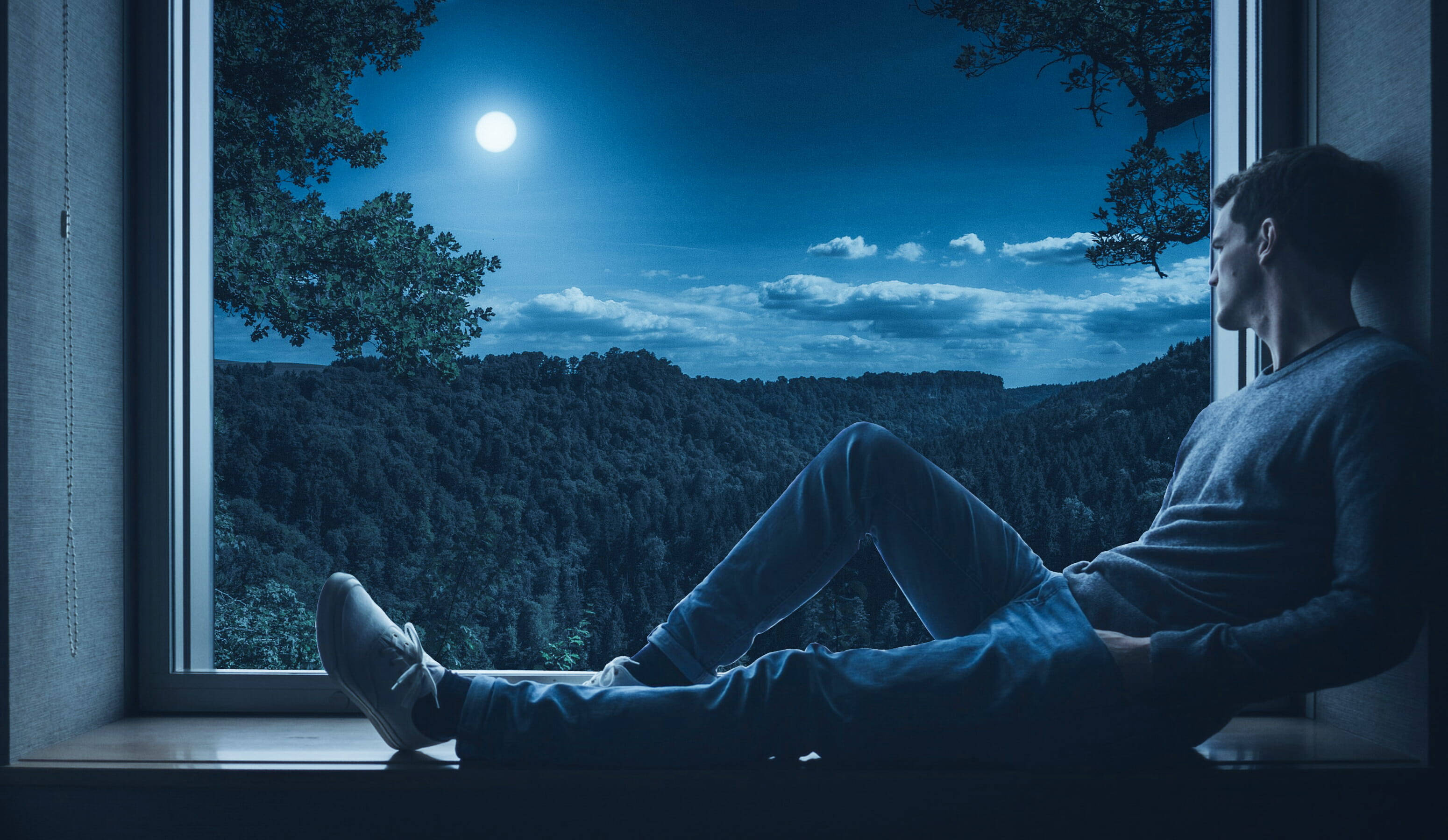 Alone 桌布 壁紙 — 一個男人坐在窗台上，凝視著深藍色夜空下月光照耀的森林。