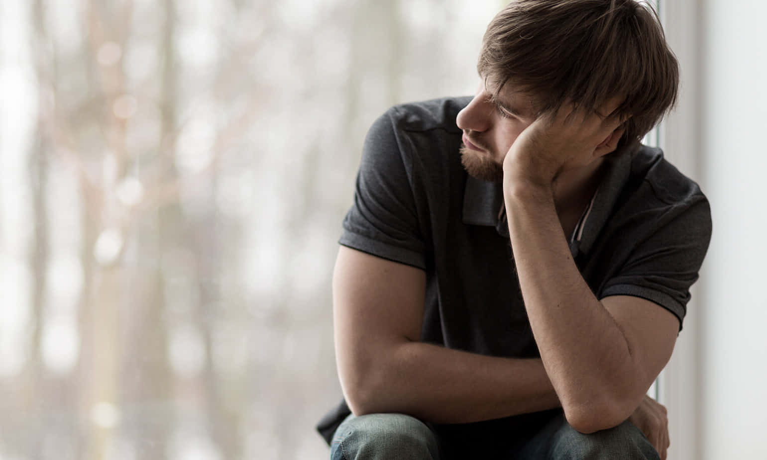 Depressed 桌布 壁紙 — 一個男人坐在窗邊，手托著頭，對著模糊的森林背景沉思。