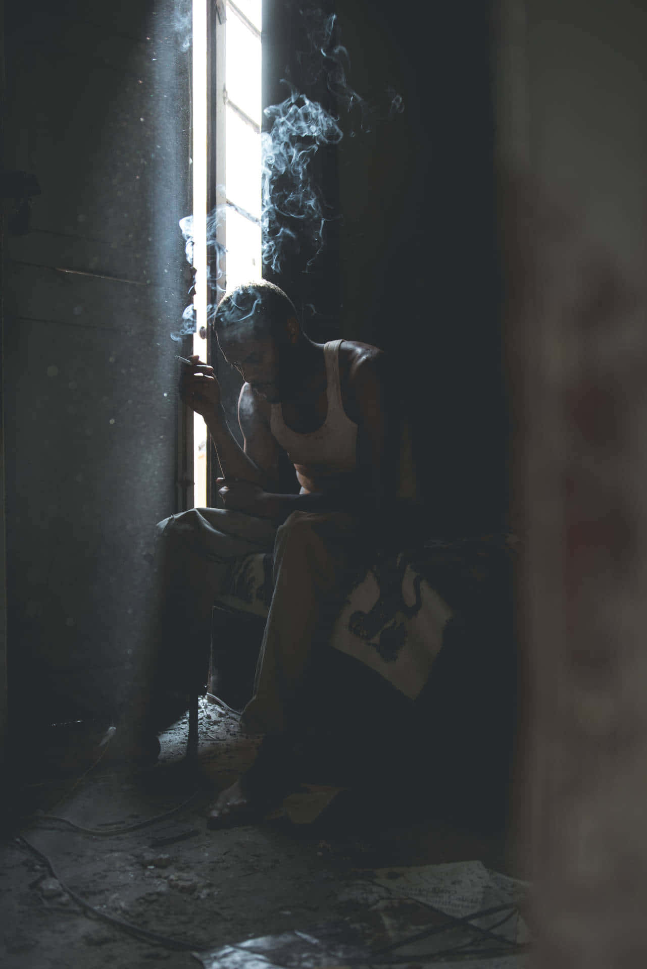 Sad Vibes 桌布 壁紙 — 一個男人坐在窗邊昏暗的光線下抽煙，煙霧在陰暗的房間裡向上繚繞。