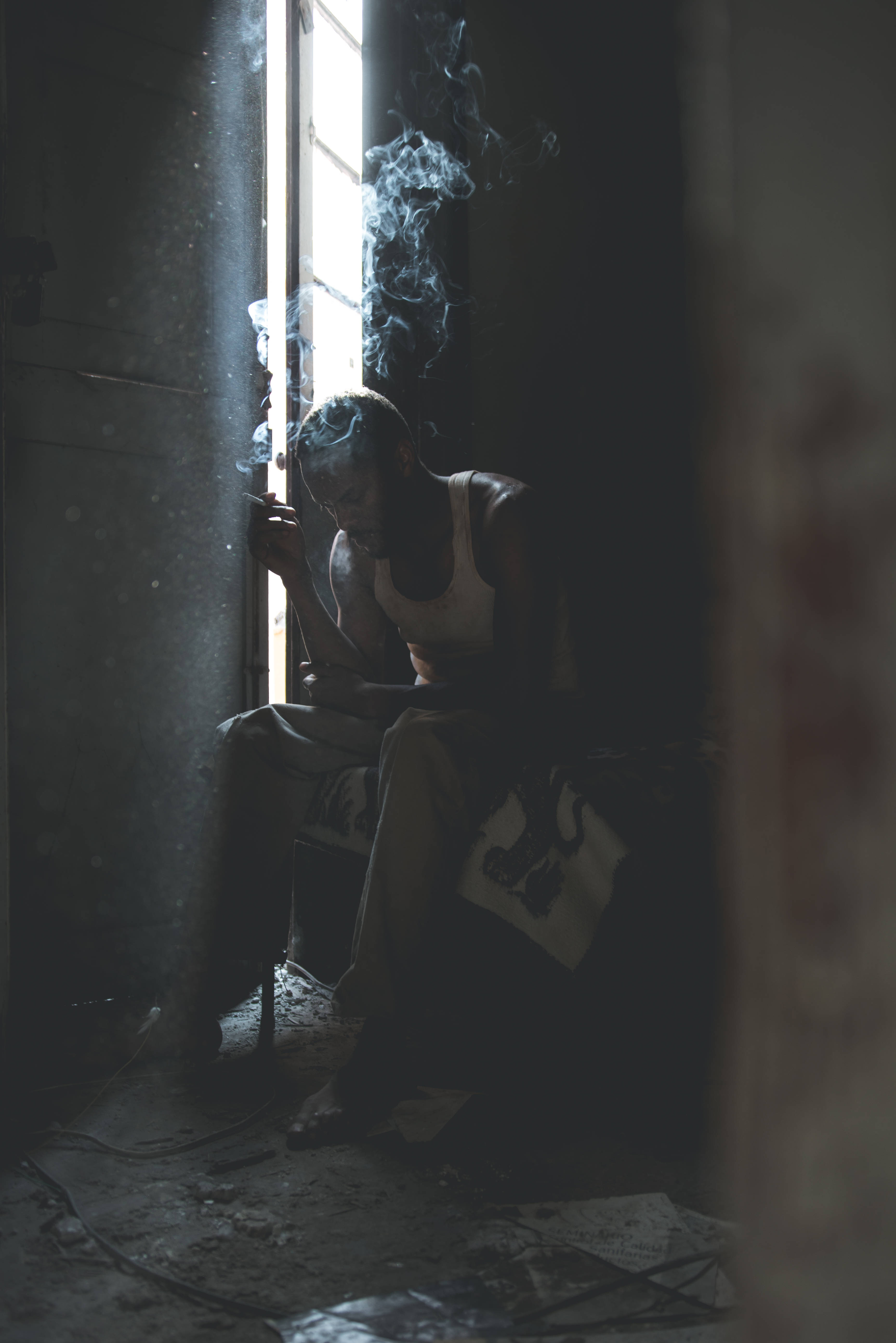 Sad Alone 桌布 壁紙 — 一個男人坐在窗邊昏暗的光線下抽煙，煙霧在佈滿灰塵的廢棄房間中向上繚繞。