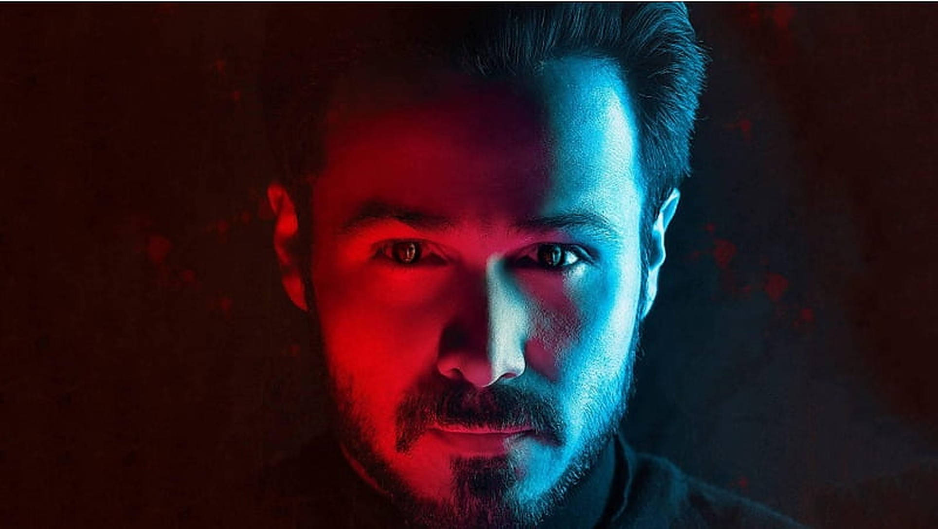 Emraan Hashmi 桌布 壁紙 — 一個男人強烈的臉龐被戲劇性的紅色和藍色燈光分割，背景為深色紋理。