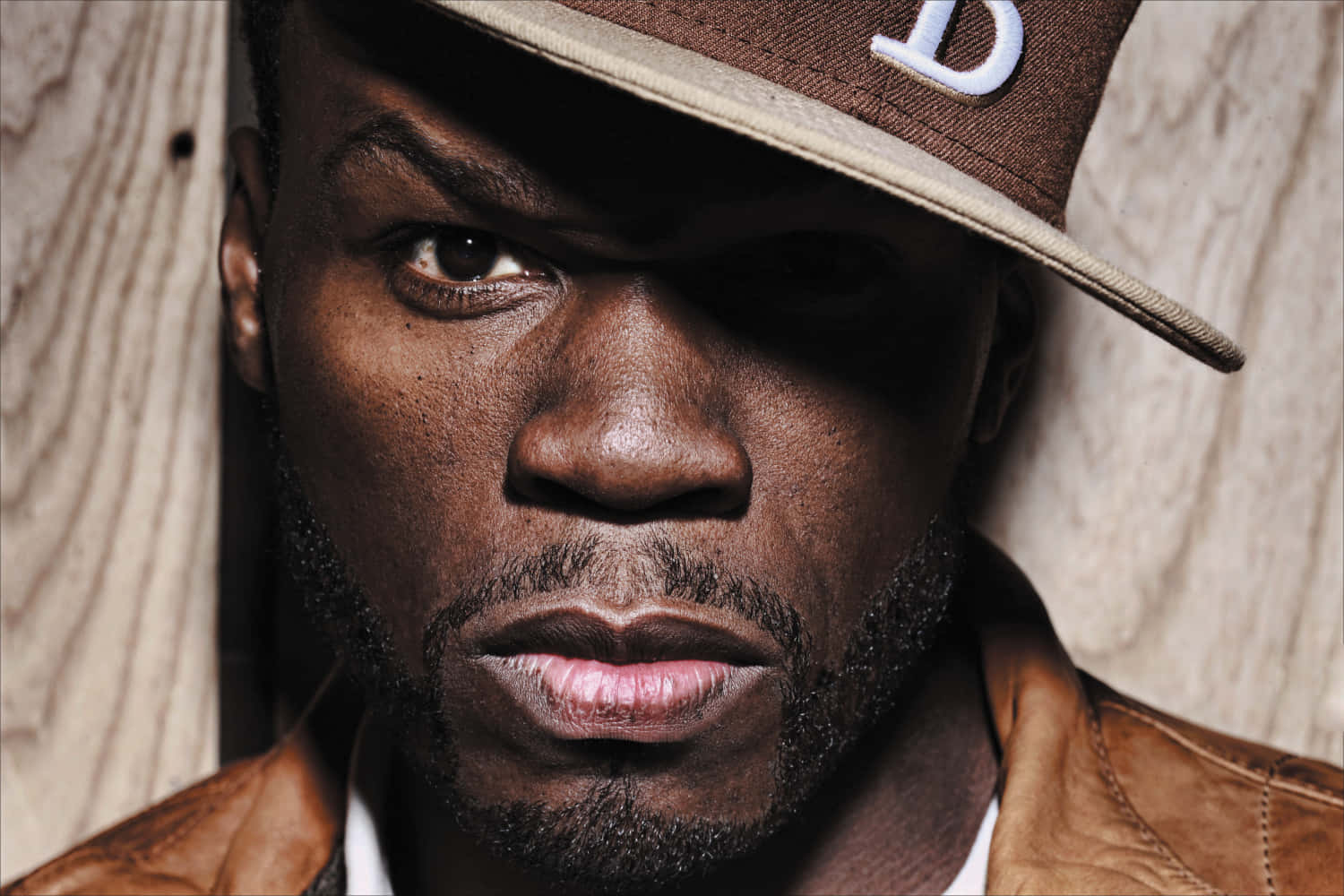 50 Cent 桌布 壁紙 — 一個男人戴著棕色帽子和皮夾克，以木質背景為襯的特寫肖像。