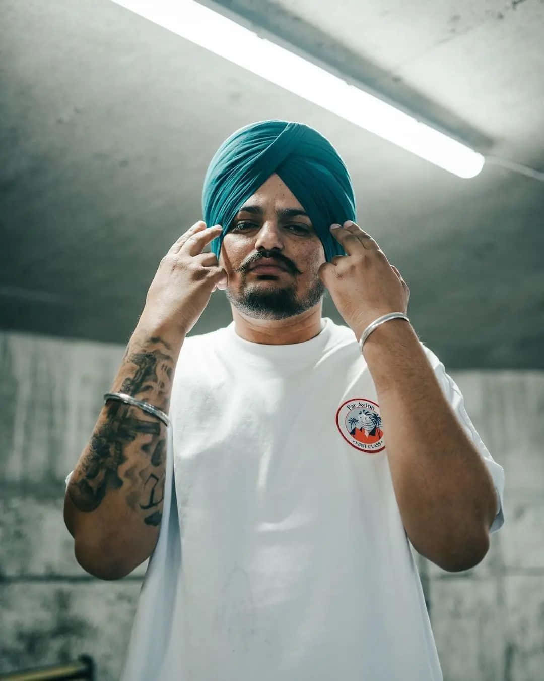 男人戴著青綠色頭巾在混凝土房間內螢光燈下調整頭巾 — Sidhu Moose Wala 壁紙