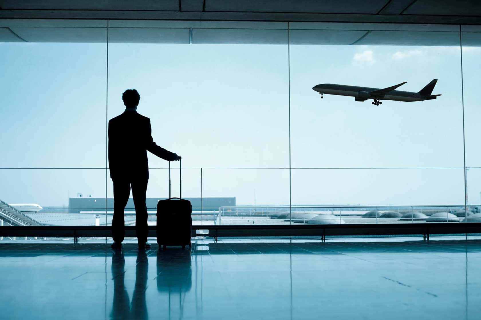 Airport 桌布 壁紙 — 一個男人提著手提箱的剪影，透過廣闊的機場窗戶看著飛機降落。