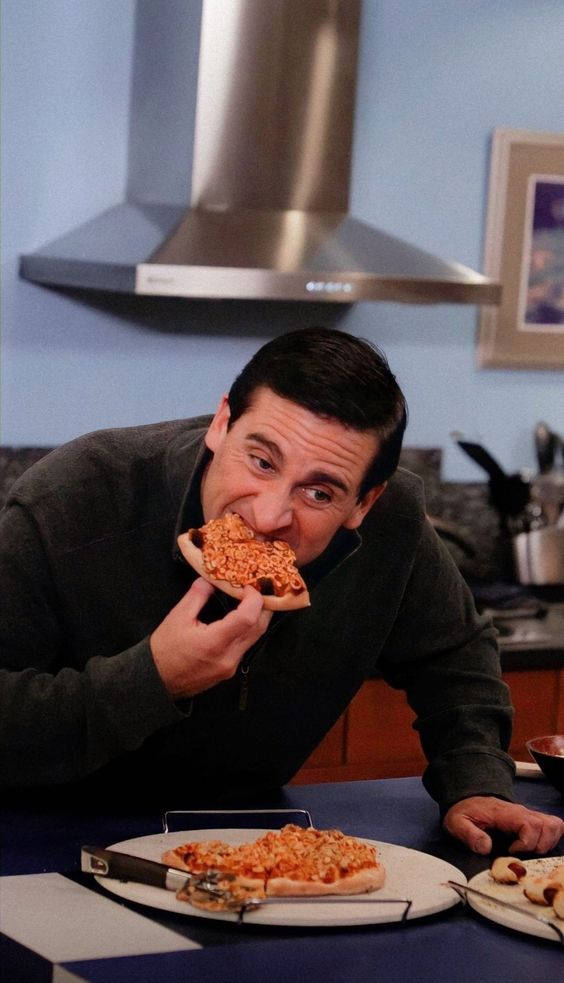 Pizza 桌布 壁紙 — 一個男人熱情地咬著一片披薩，廚房裡有一個不鏽鋼抽油煙機在他上方。