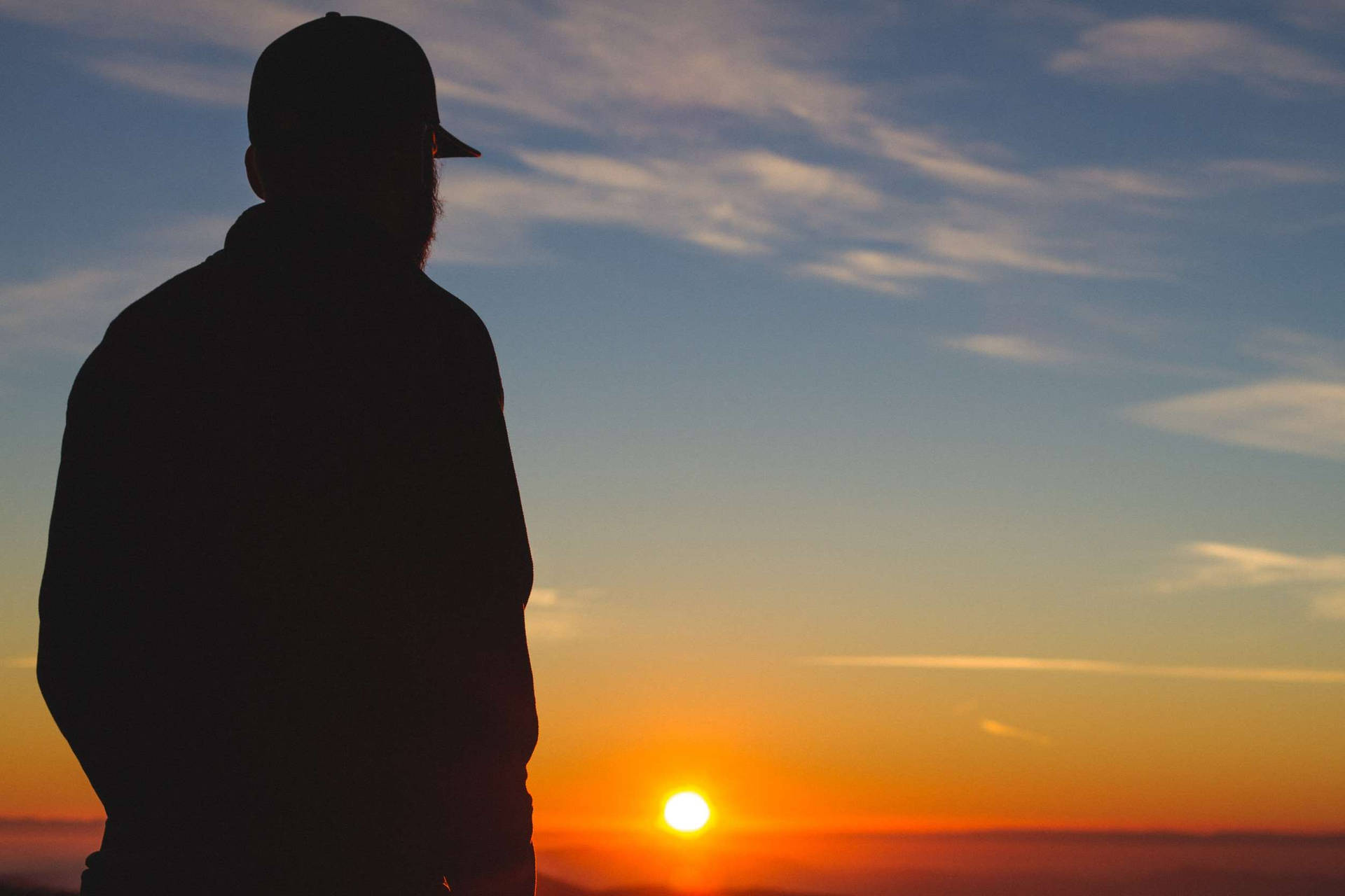Silhouette 桌布 壁紙 — 一個男人的剪影站著凝視著充滿活力的日落，天空呈現橙色和藍色。