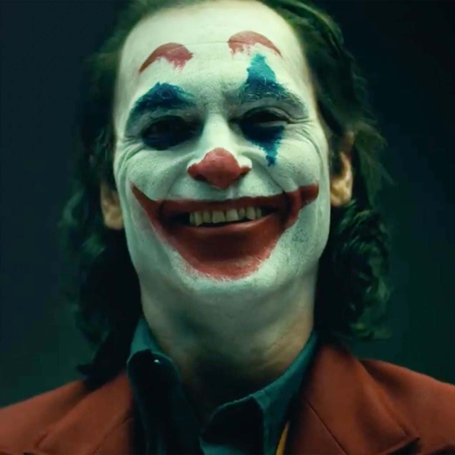 Joker Laughing 桌布 壁紙 — 一個男人的特寫，他有白色臉部彩繪、紅色嘴唇和藍色眼淚，在黑暗環境中瘋狂地微笑。