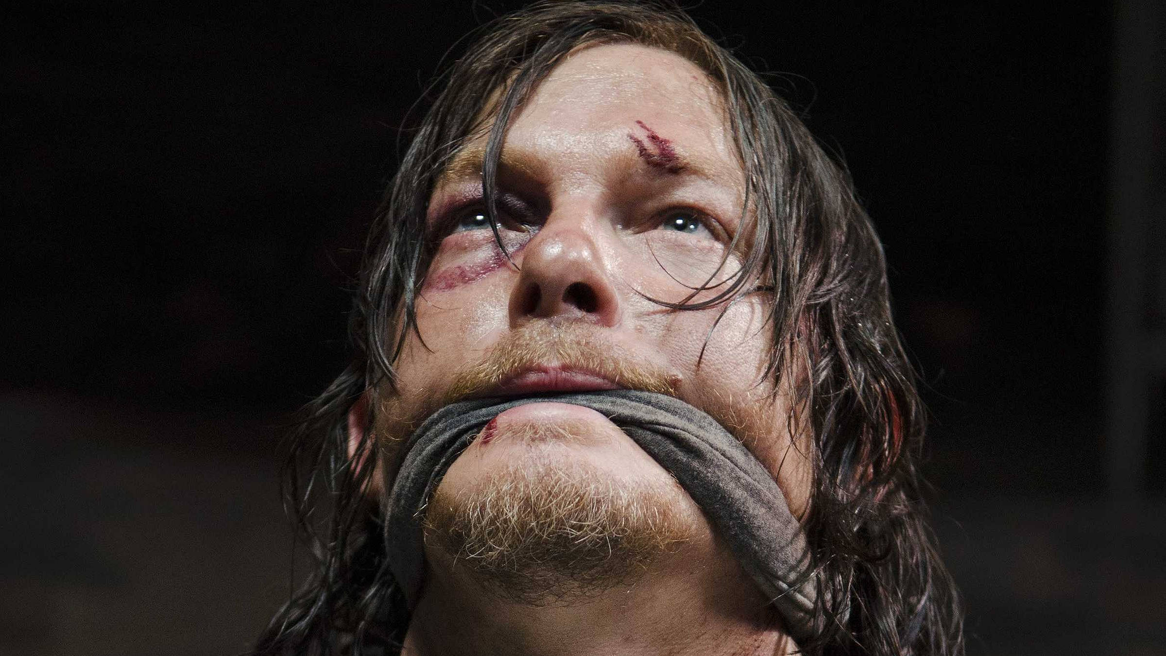 Walking Dead Daryl 桌布 壁紙 — 一個男人的特寫，他的臉血跡斑斑，嘴巴被布塞住，背景是黑色。