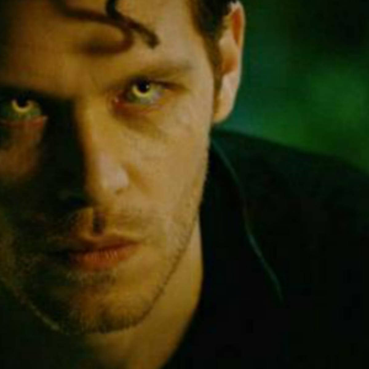 Vampire Diaries 桌布 壁紙 — 一個男人的特寫，在昏暗的綠色燈光下，他有強烈的發光眼睛和額頭上的深色標記。