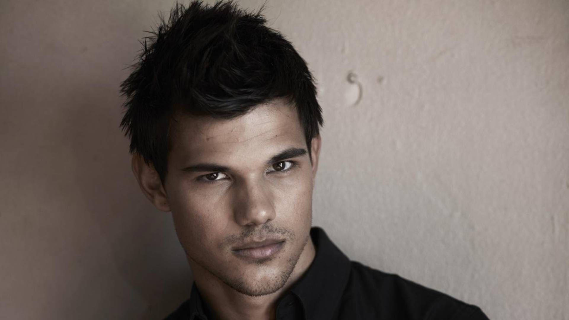 Taylor Lautner 桌布 壁紙 — 一個男人的特寫肖像，他有深色刺蝟頭和強烈的眼神，背景是有紋理的米色牆。