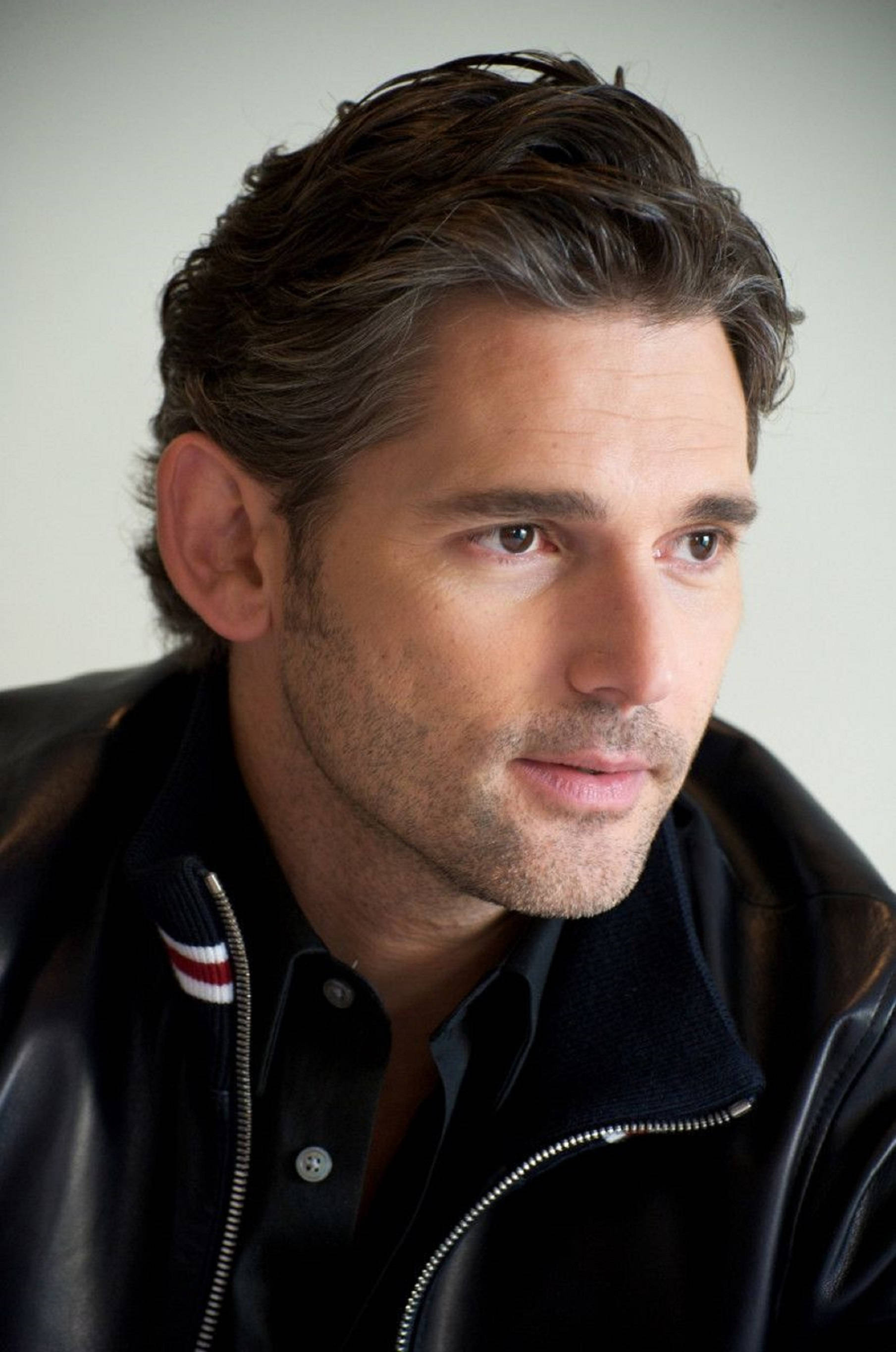 actor 桌布 壁紙 — 一個男人的特寫肖像，他有深色紋理頭髮和鬍渣，穿著黑色皮夾克，背景簡單。