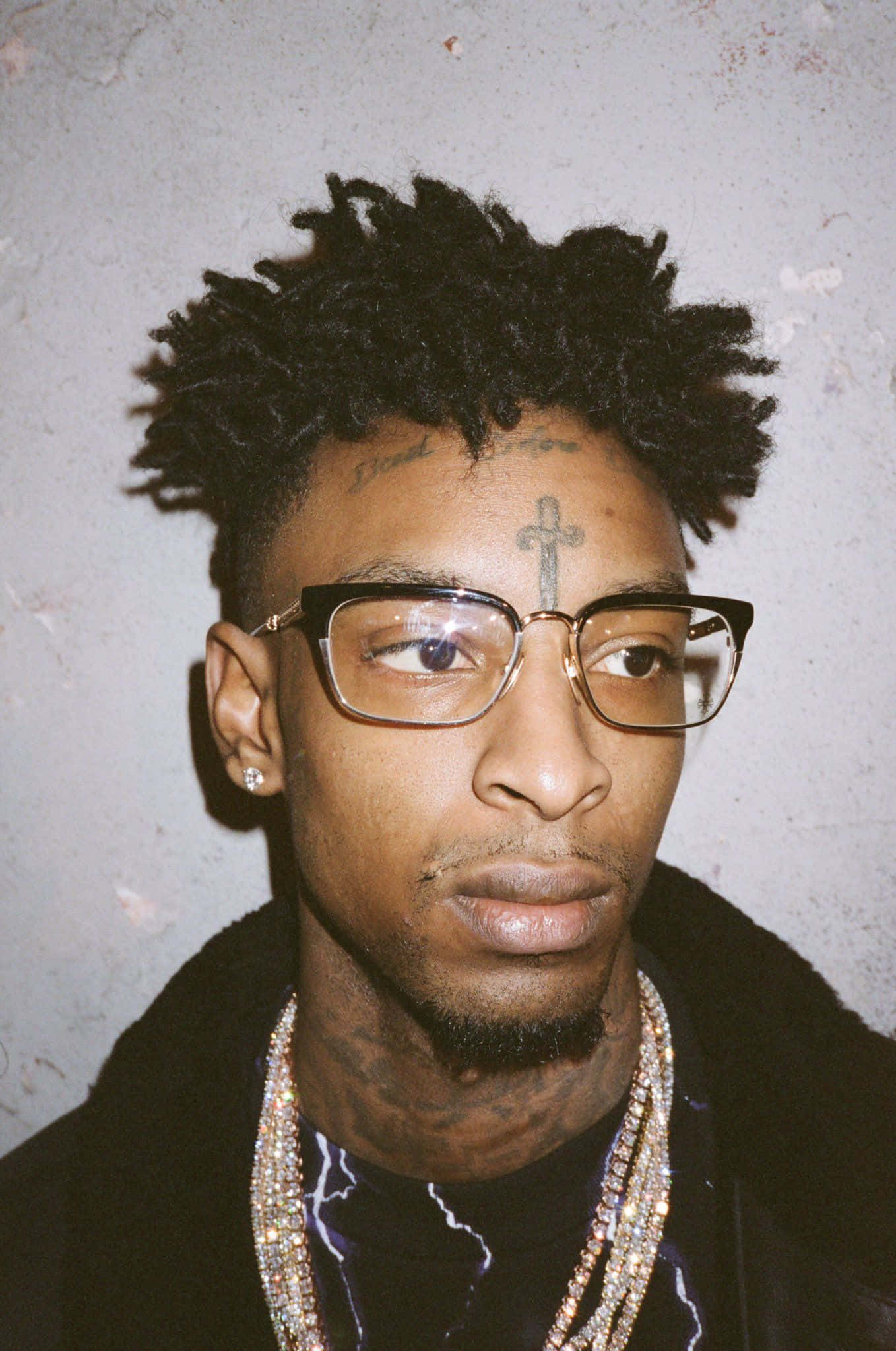 21 Savage 桌布 壁紙 — 一個男人的特寫肖像，他有辮子頭和眼鏡，背景是有紋理的灰色牆壁。