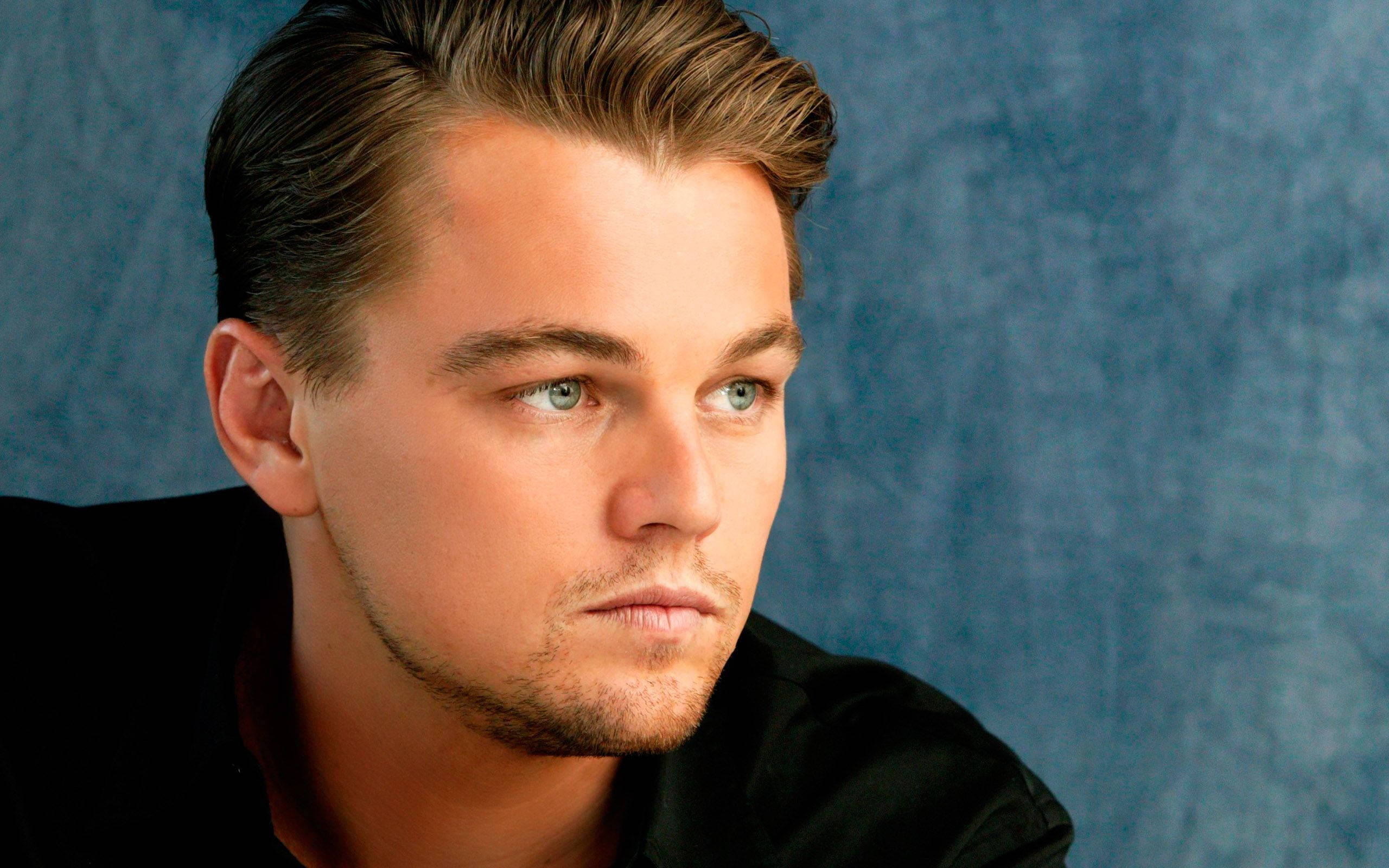 Dicaprio 桌布 壁紙 — 一個男人的特寫肖像，他有造型的頭髮和強烈的藍色眼睛，背景是帶紋理的藍色。