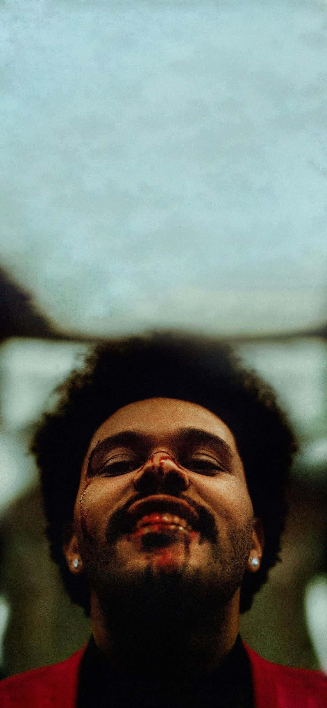 The Weeknd After Hours 桌布 壁紙 — 一個男人的特寫肖像，他閉著眼睛，露出開心的笑容，穿著紅色外套，背景柔和模糊。
