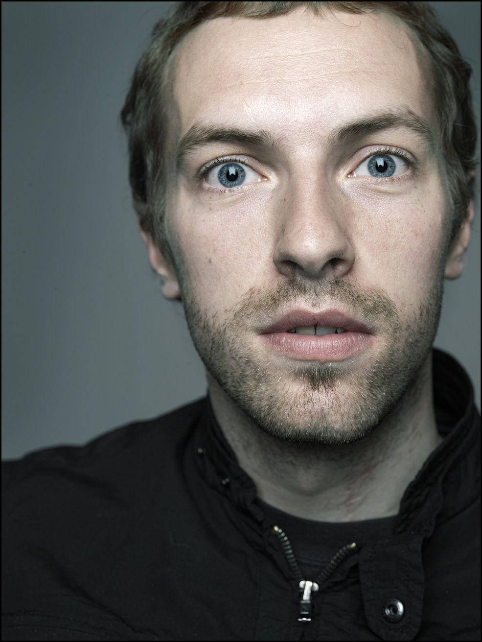 Chris Martin 桌布 壁紙 — 一個男人的特寫肖像，擁有引人注目的藍色眼睛和鬍渣，背景是純灰色。