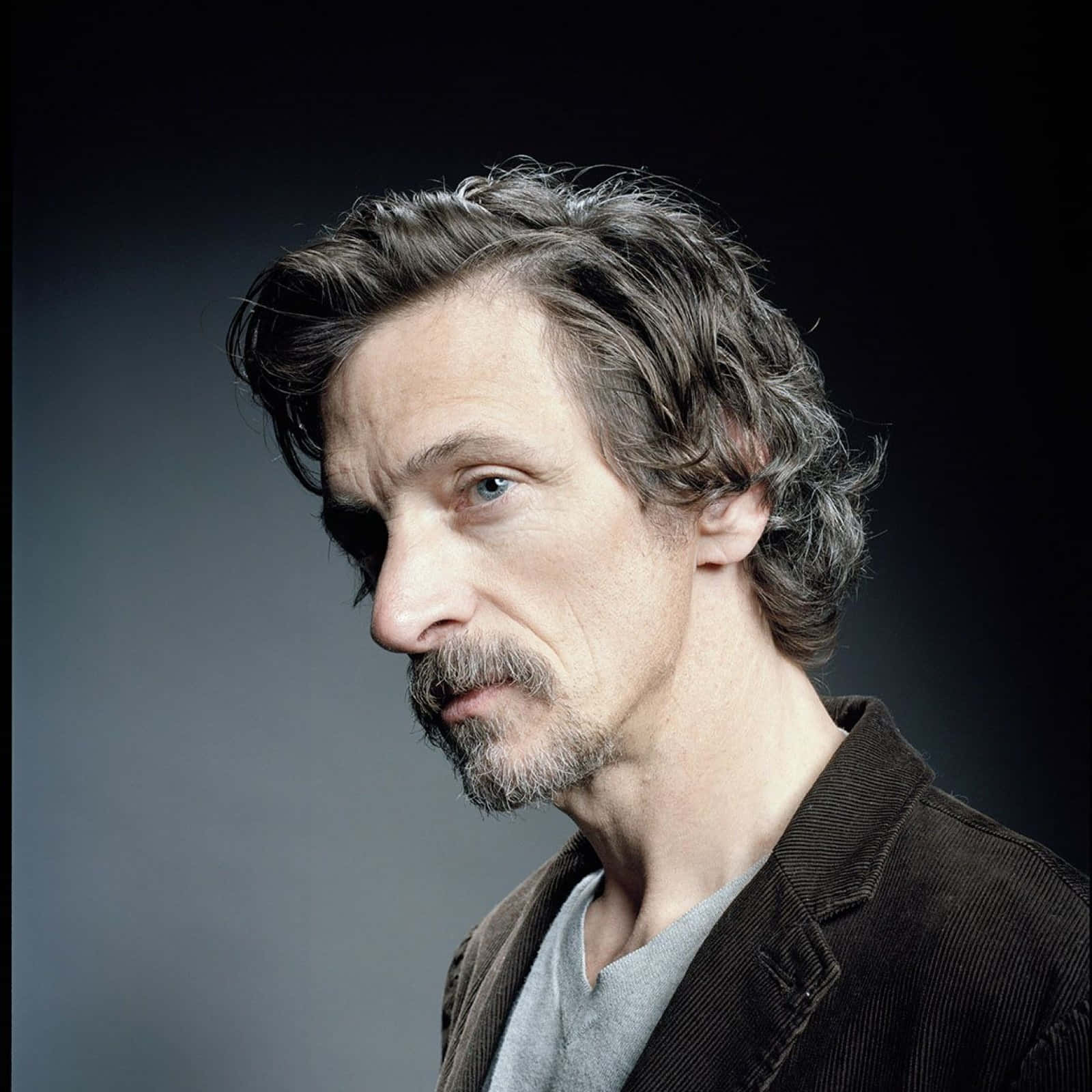 John Hawkes 桌布 壁紙 — 一個男人的近距離肖像，他有灰白頭髮和鬍鬚，看向旁邊，背景是深色漸變。