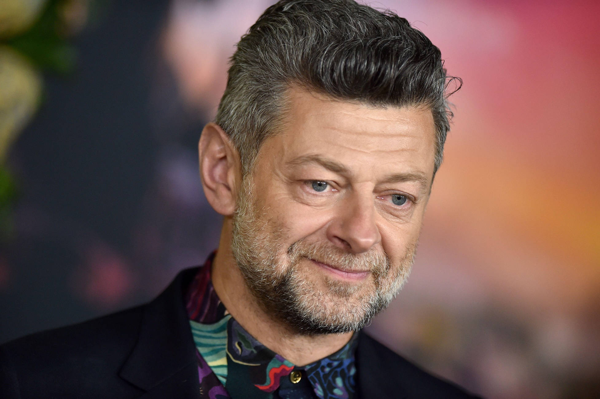 actor 桌布 壁紙 — 一個男人的近距離肖像，他有灰白頭髮和鬍鬚，穿著深色西裝和色彩繽紛的圖案襯衫，背景模糊而充滿活力。