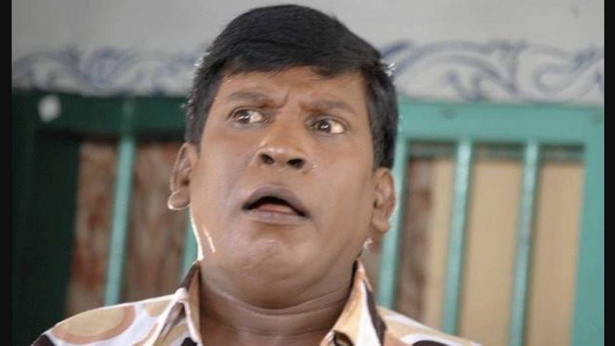 Vadivelu 桌布 壁紙 — 一個男人睜大眼睛、張開嘴巴，震驚地向上看，背景是有圖案的牆和綠色欄杆。