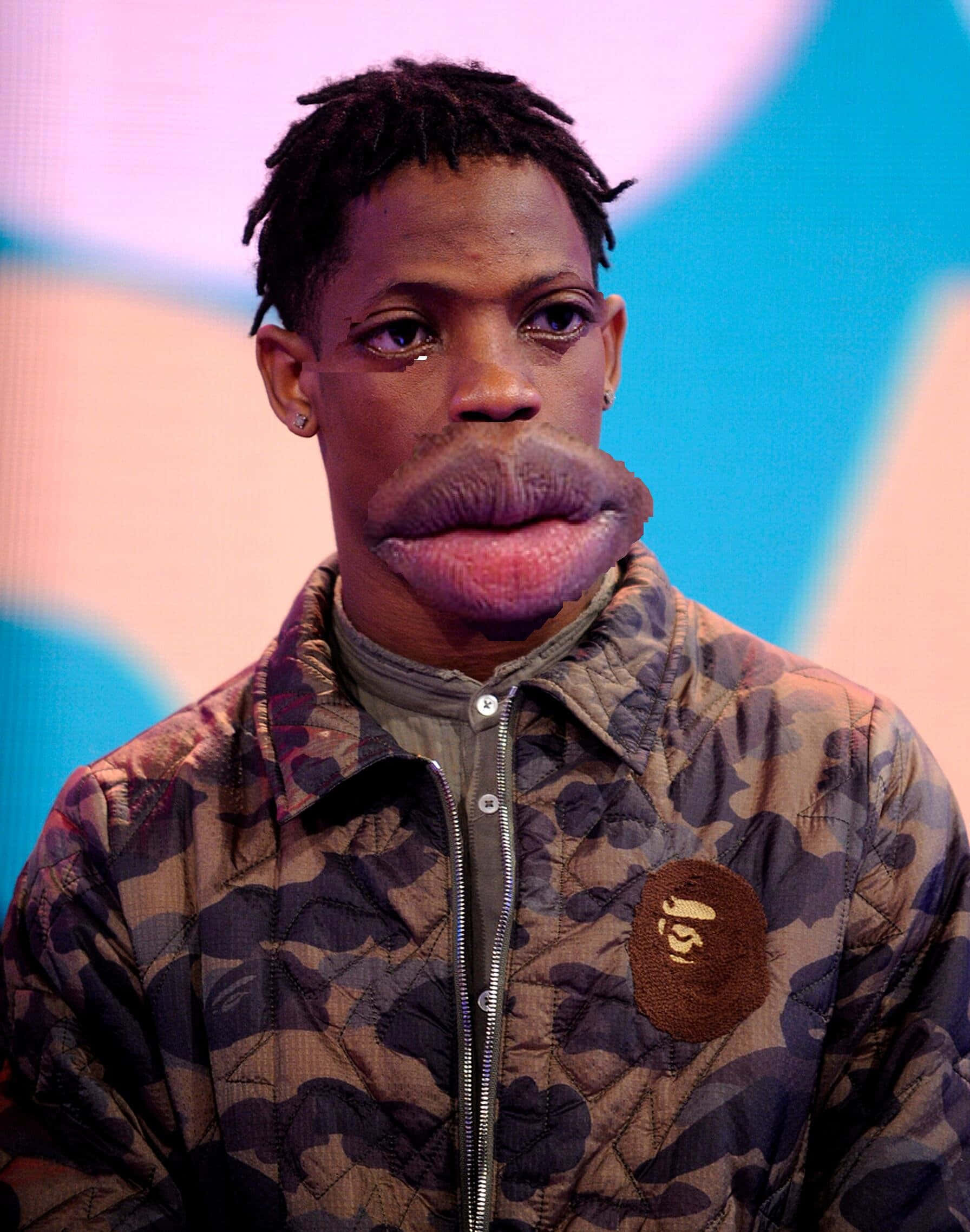 Travis Scott Funny 桌布 壁紙 — 一個男人穿著帶有BAPE標誌的迷彩外套，數位修改過的超大嘴巴，眼神銳利地凝視。